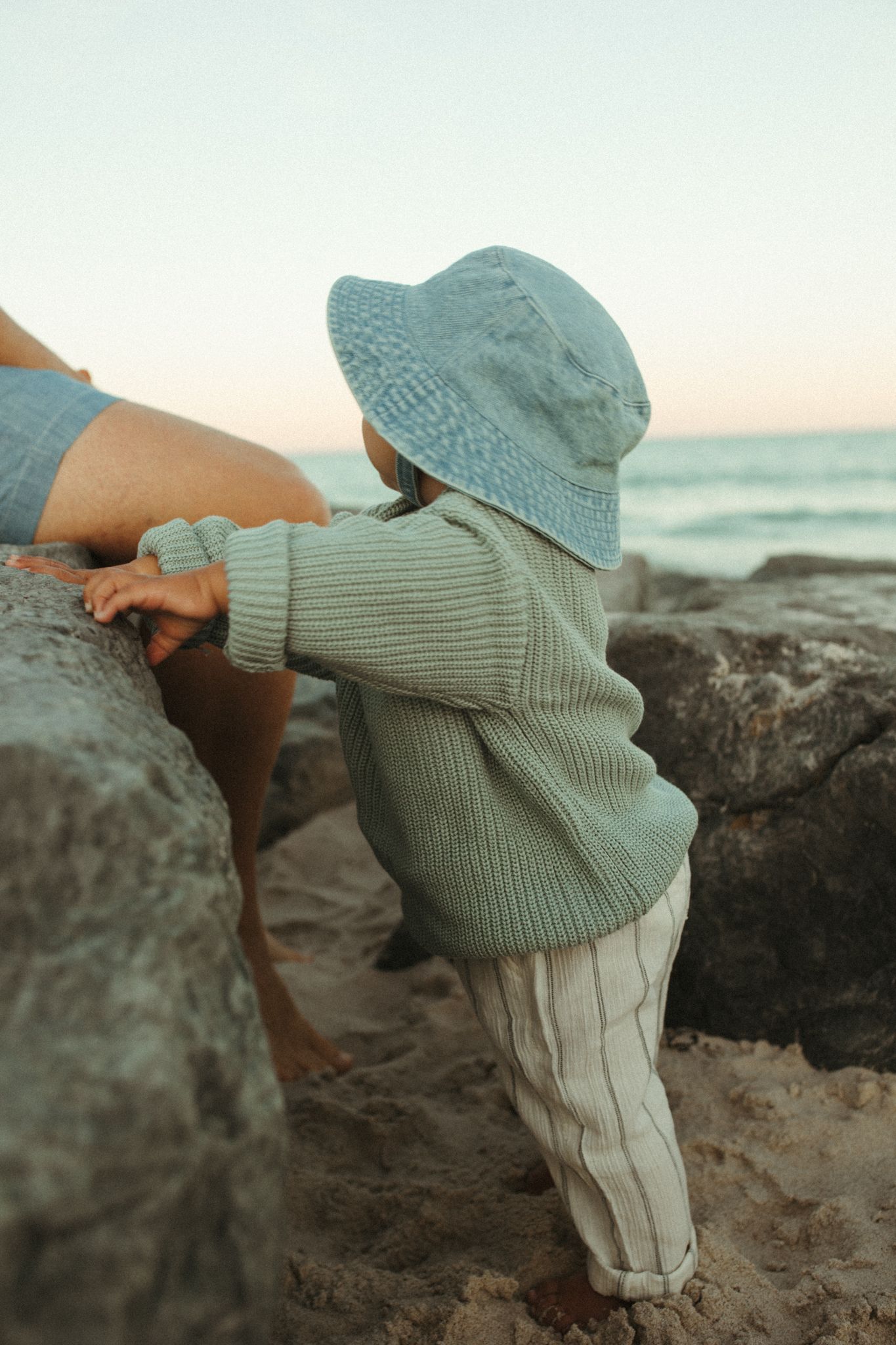 Child in blue hat exploring rocks at the beach.