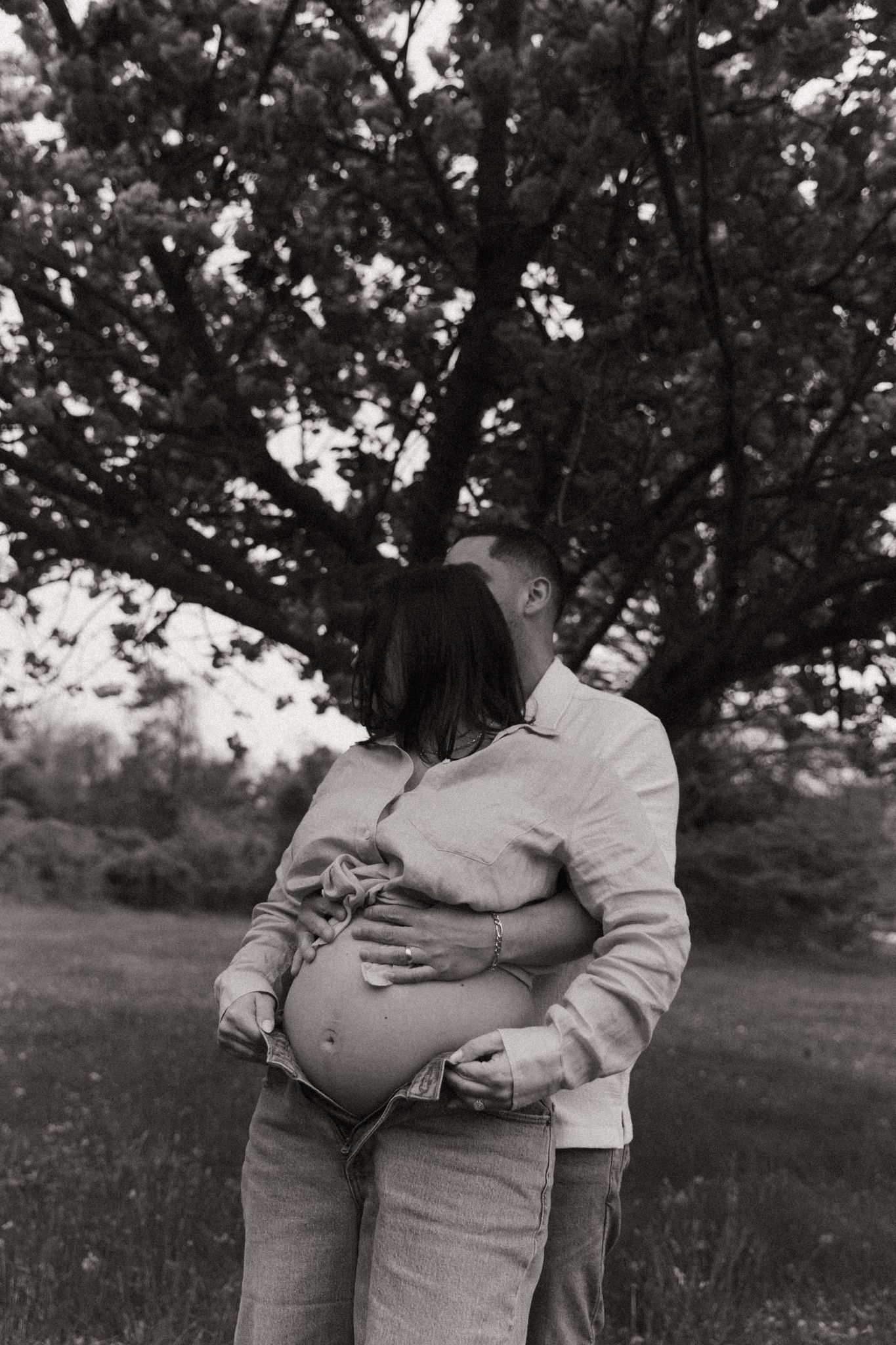 Black and white intimate maternity photo under blooming trees.