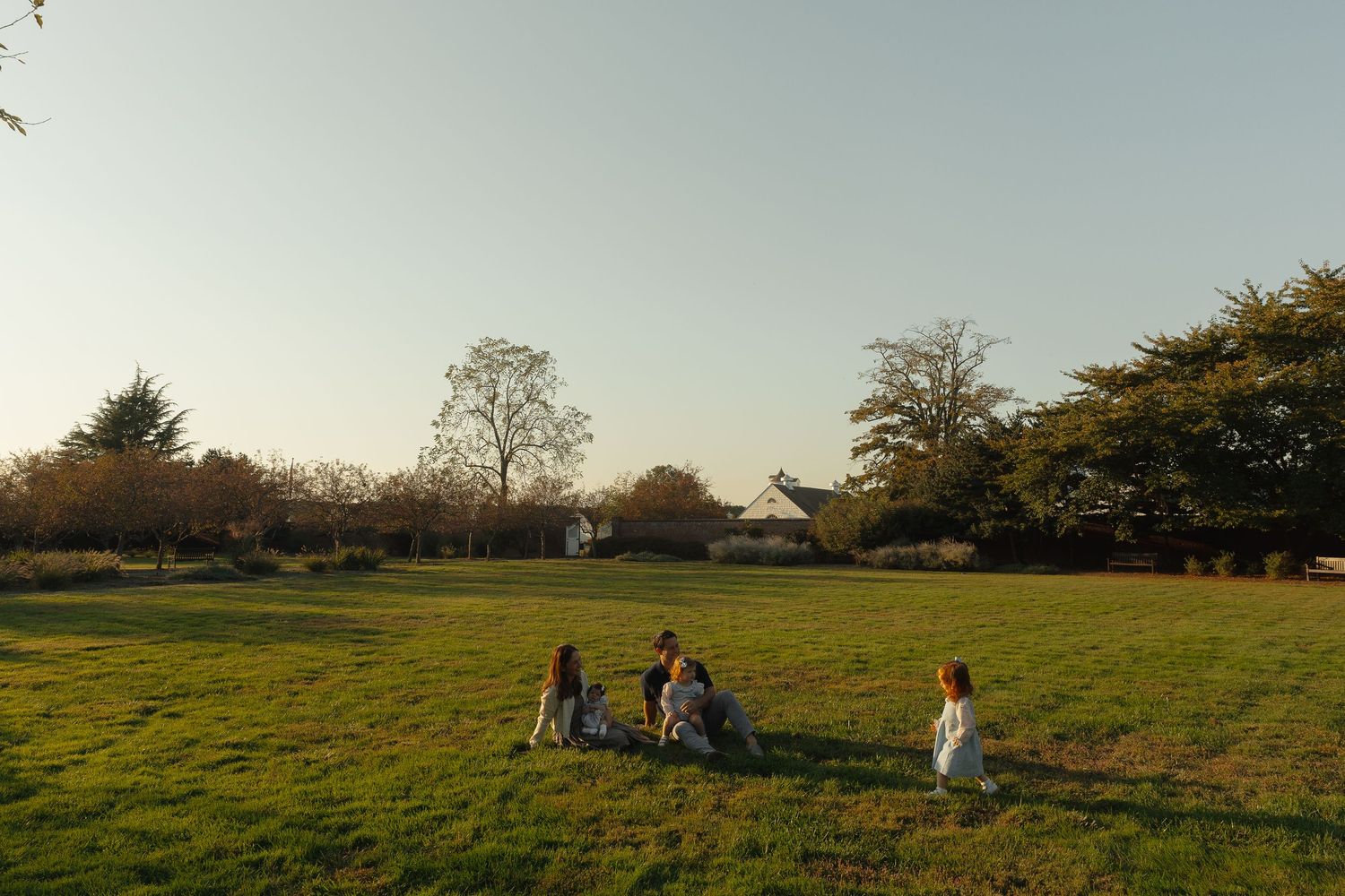 Family with young children sitting and playing together in a sunny open green field.