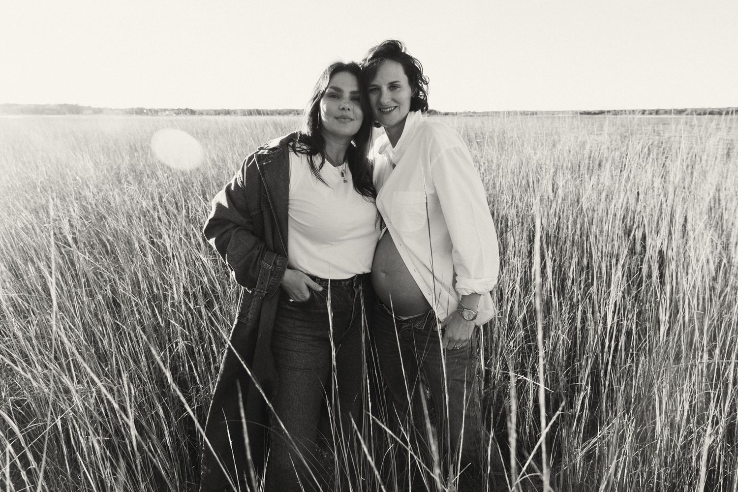 Two women smiling together in a vast grassy field, captured in a timeless black and white portrait.