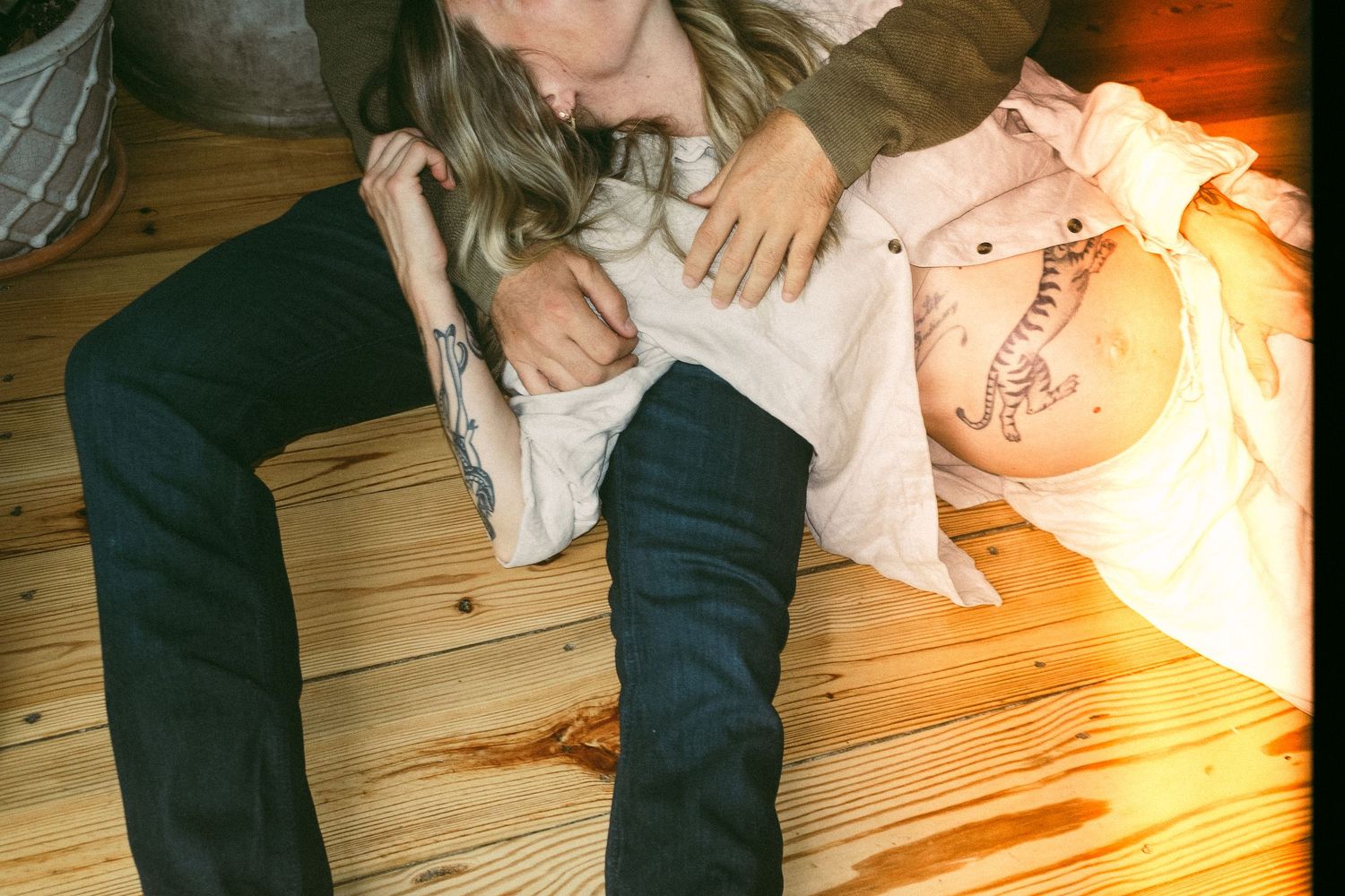 Mother sitting on wooden floor cradling and cuddling her young baby in warm natural light.