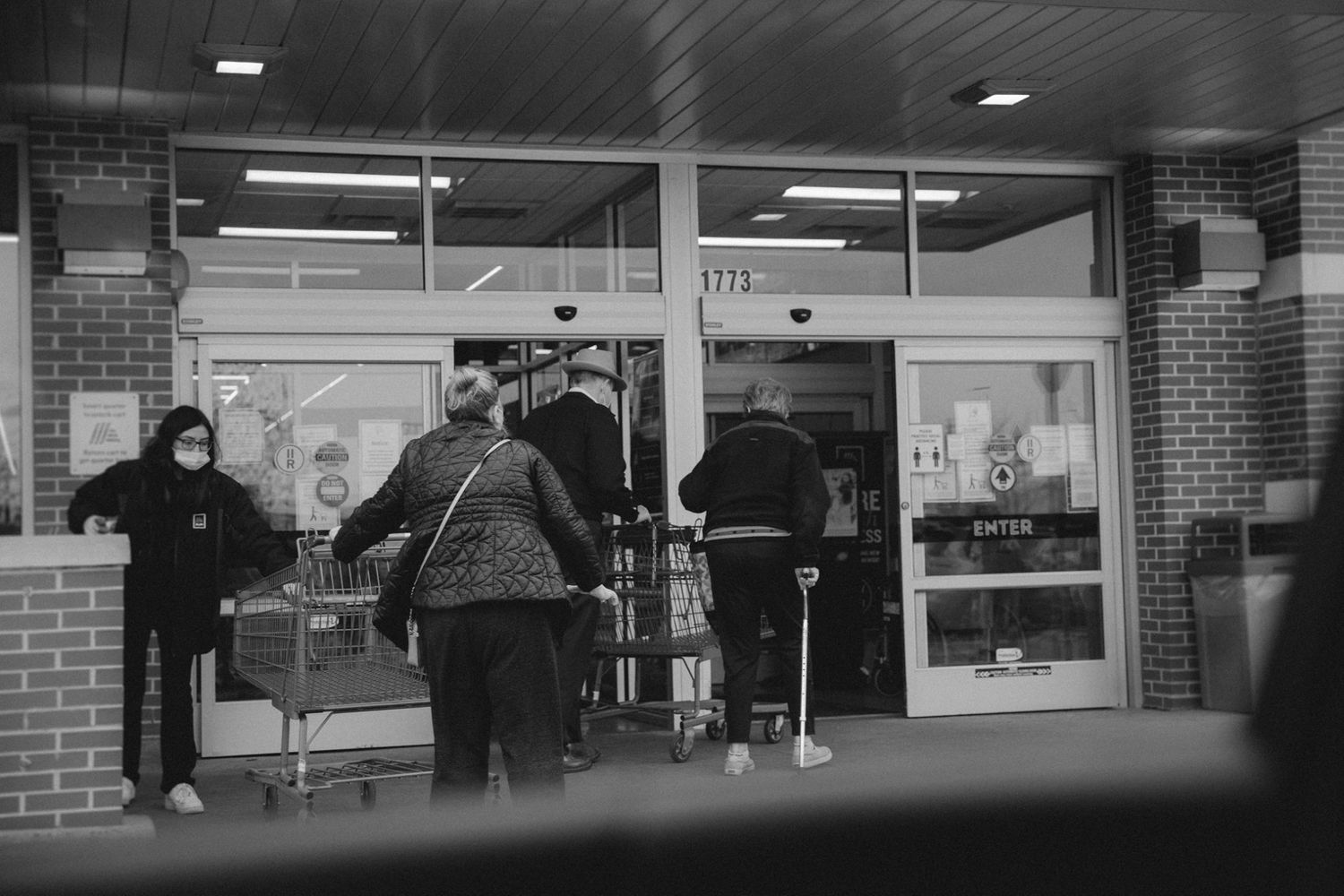 People entering a retail store entrance captured in black and white.