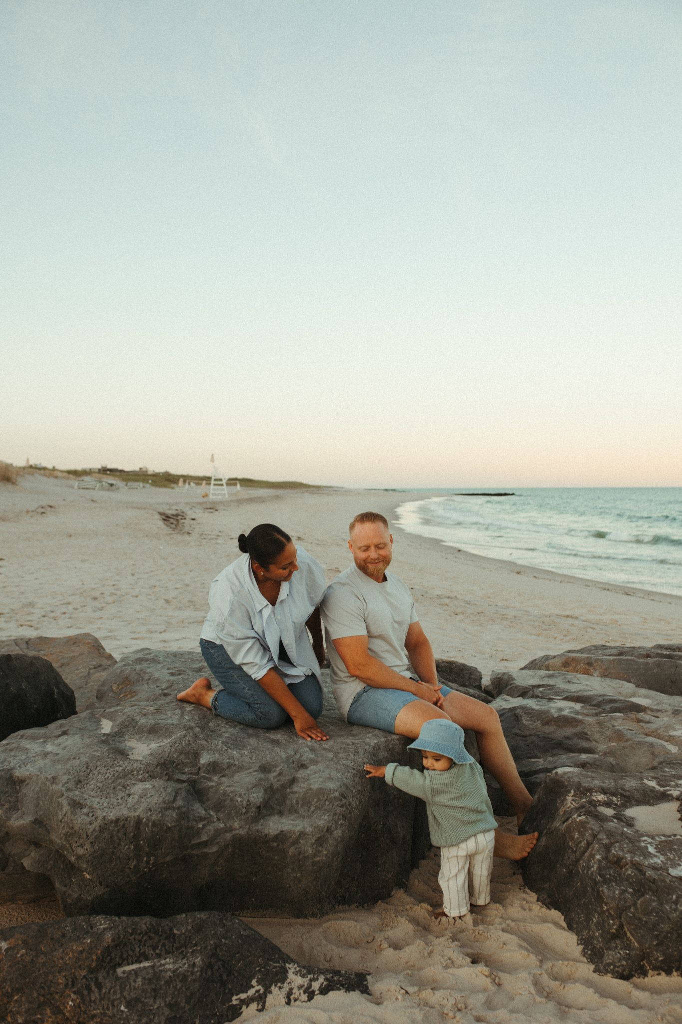 People exploring rocky formations along the beach at dusk.