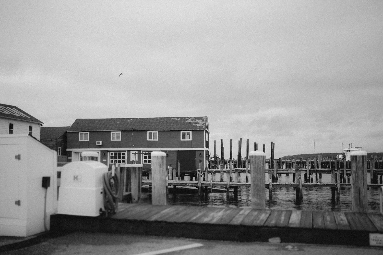 A monochrome image of a waterfront dock with buildings and boats in overcast weather.