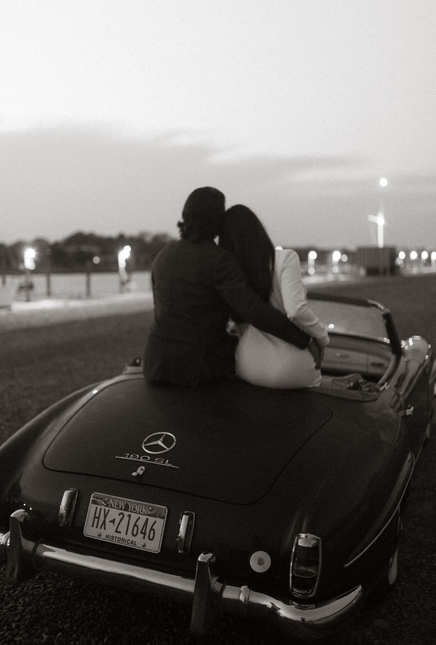 Vintage black car photographed at dusk with city lights in the background.
