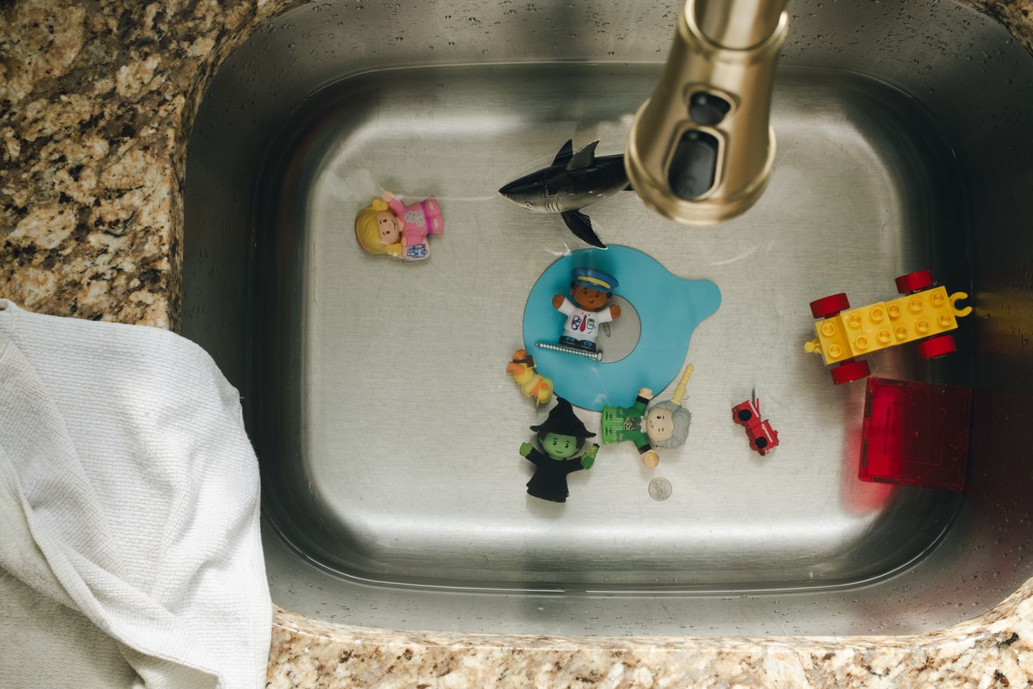 A stainless steel kitchen sink filled with soapy water and colorful bath toys floating on the surface.
