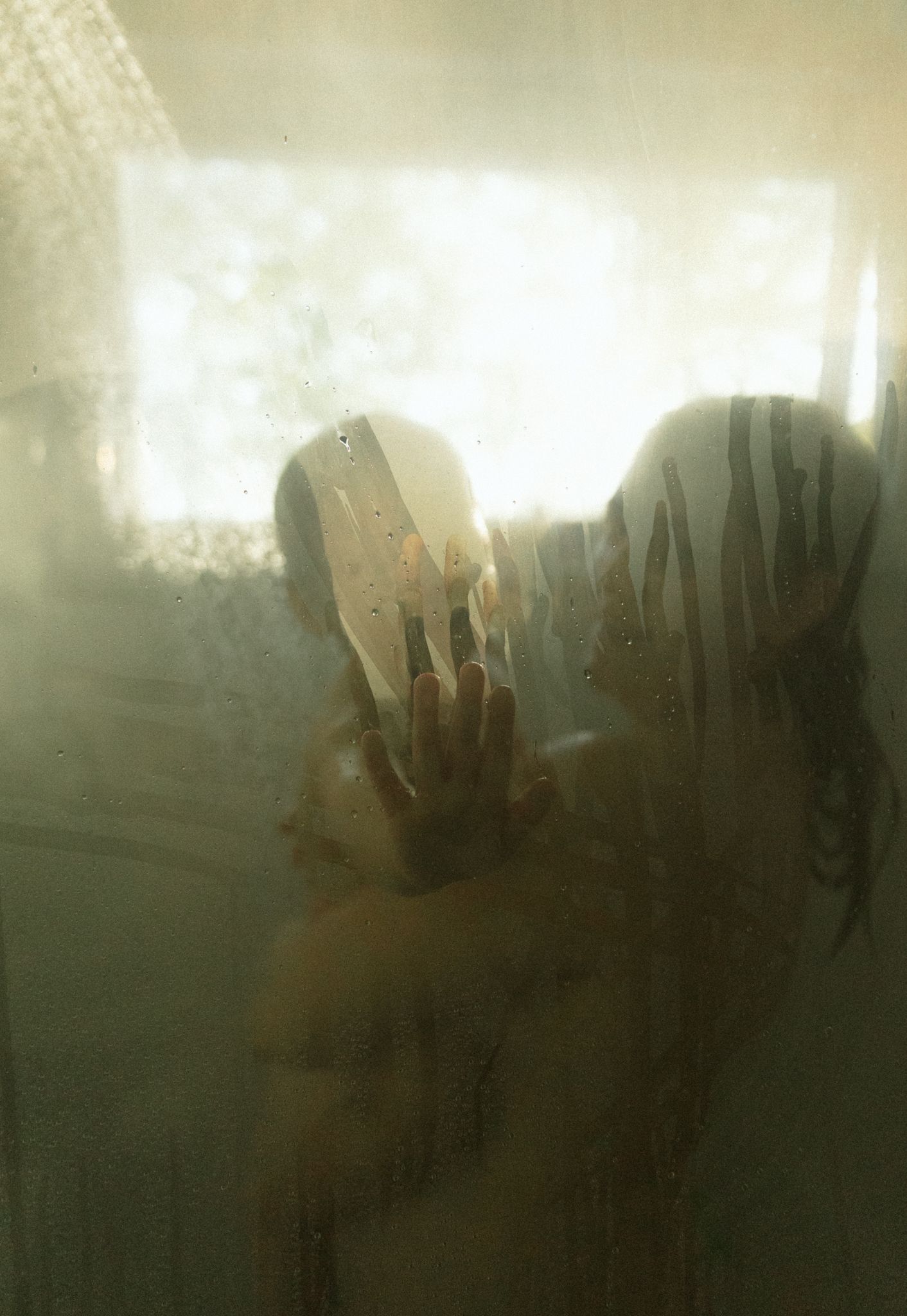 Silhouette of a person visible through a steamy frosted shower door with warm golden light.