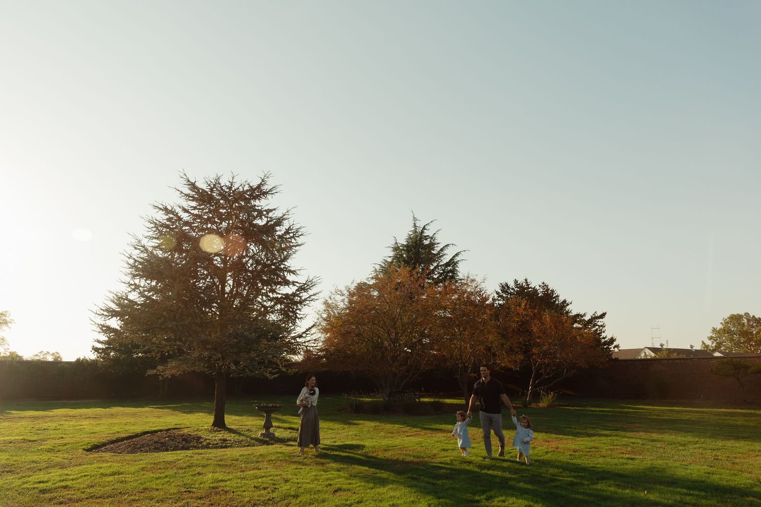 Family walking together in a sunlit autumn park with golden trees and green grass during sunset.