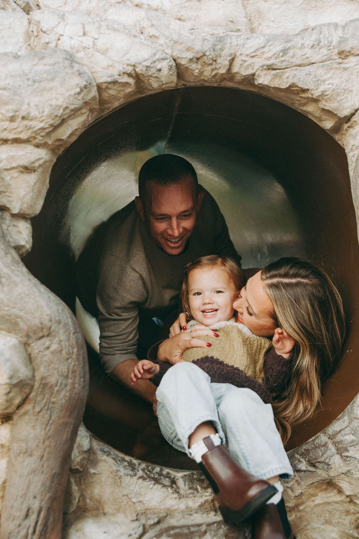 A family shares a playful moment inside a tunnel at a playground.