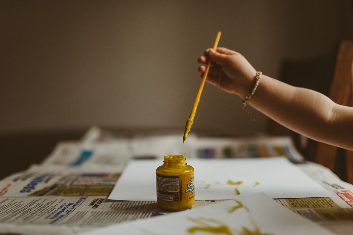 Close-up of hands painting with yellow paint on paper.