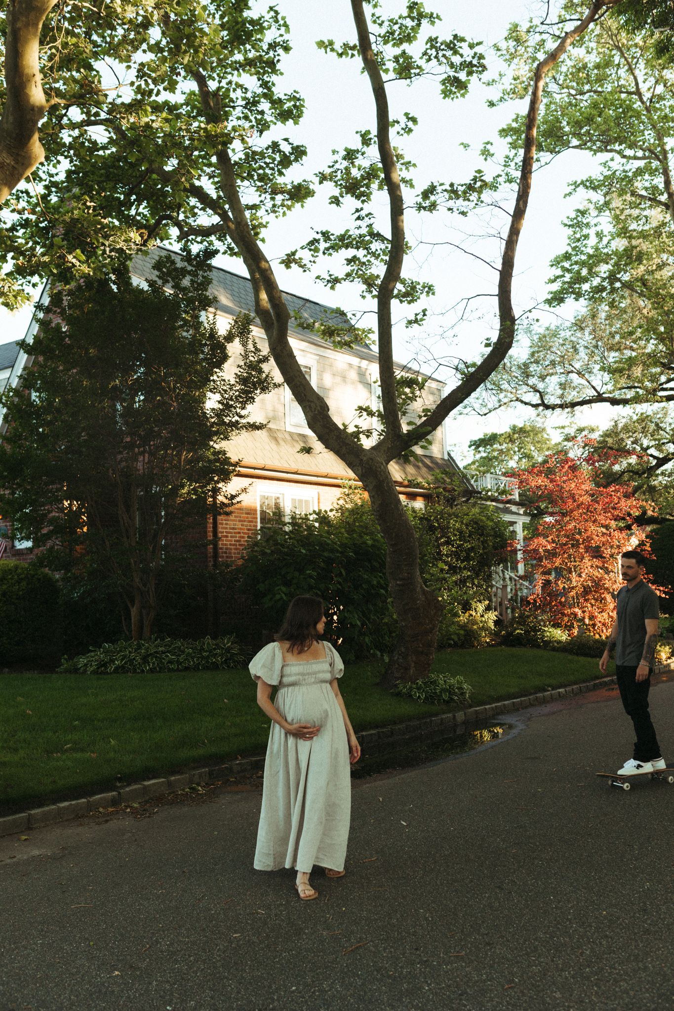 A couple sharing moments together on a tree-lined pathway near brick houses.