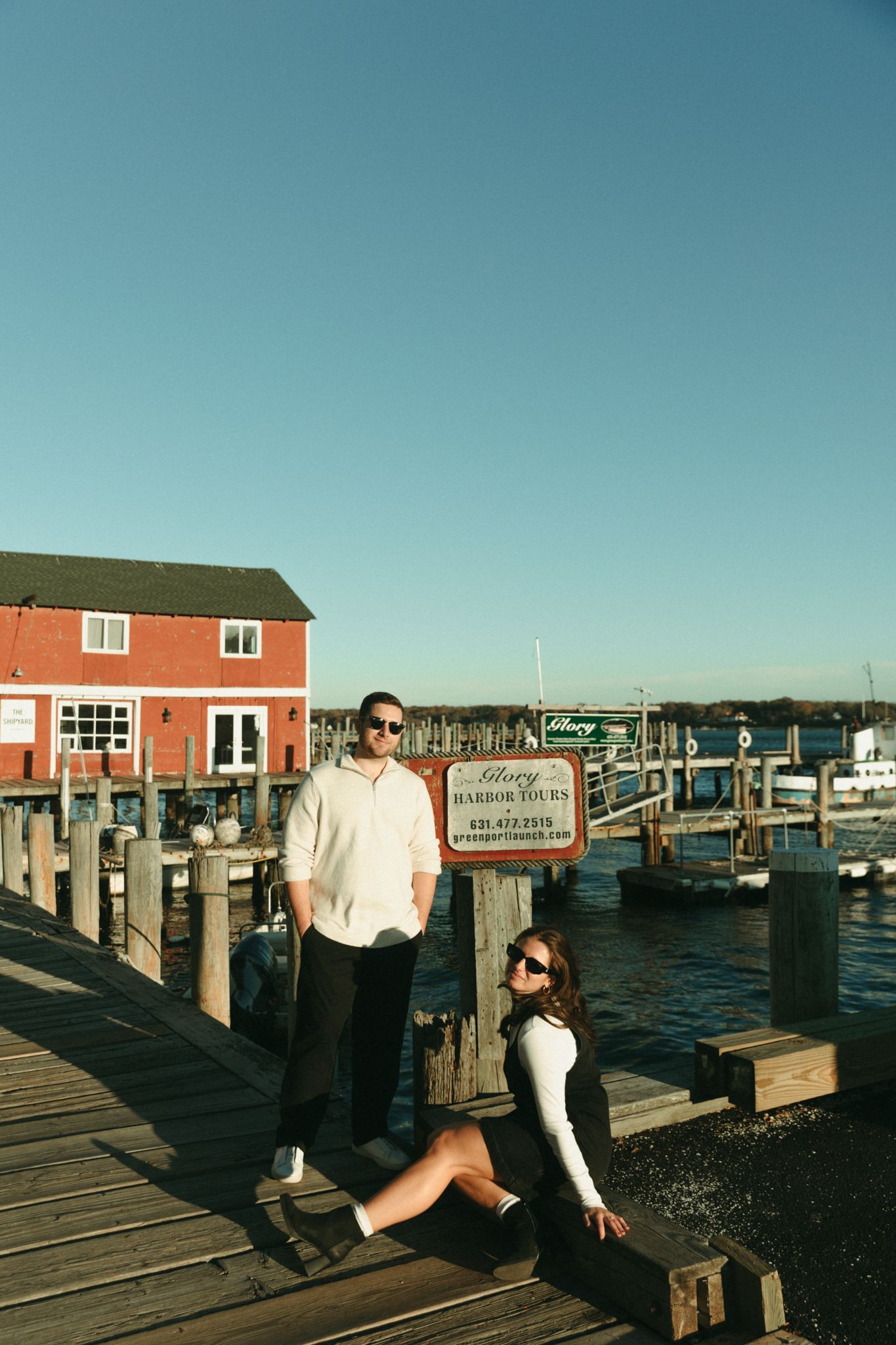 People enjoying a sunny day on a wooden dock with red buildings in the background.