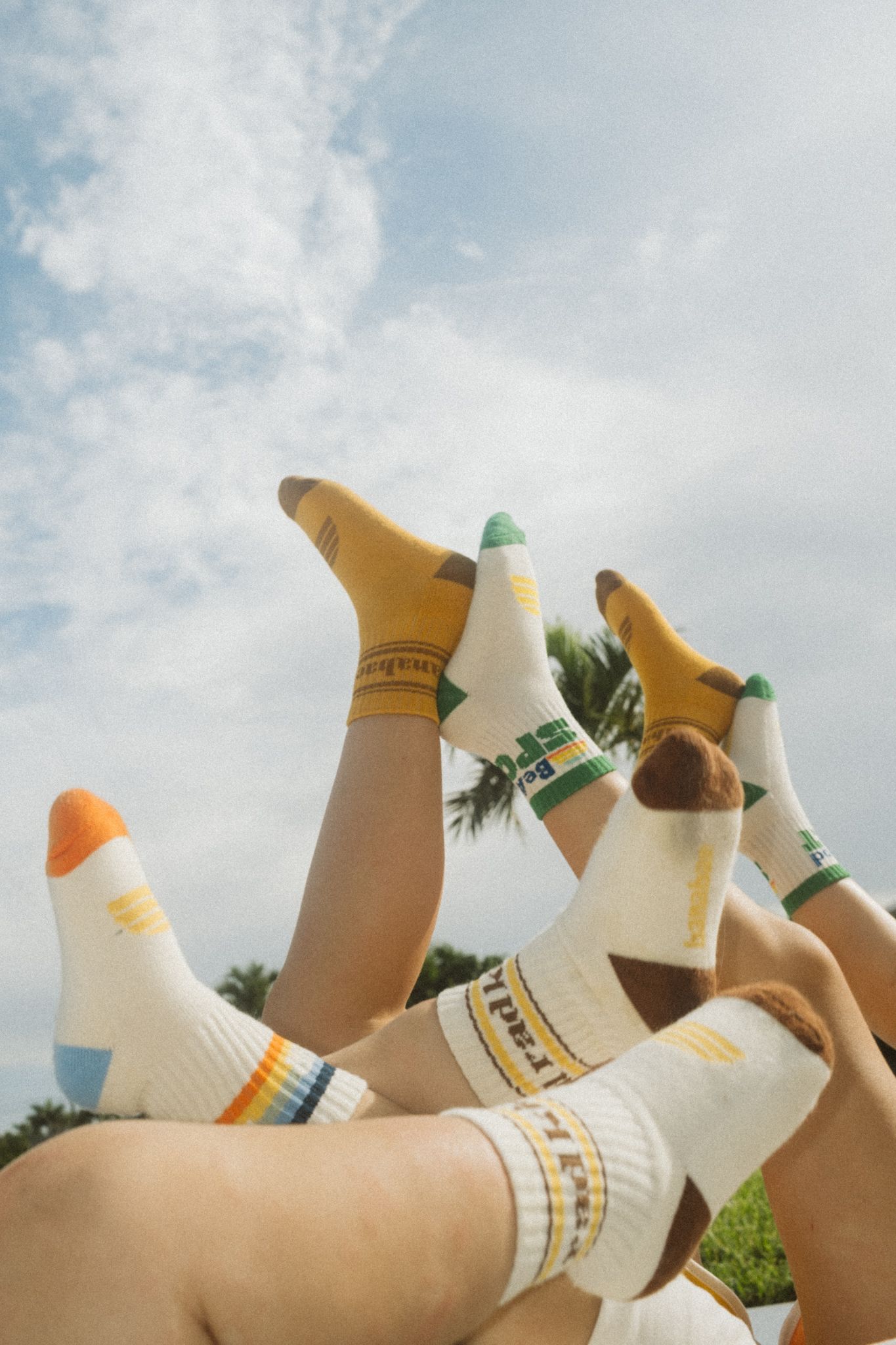 Multiple pairs of legs raised in the air wearing colorful branded crew socks against a blue sky backdrop.