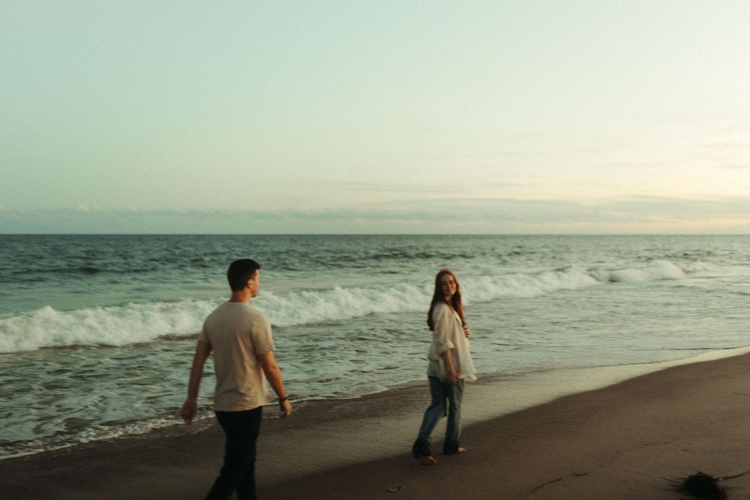 A couple dances along an empty beach with gentle waves in the background.