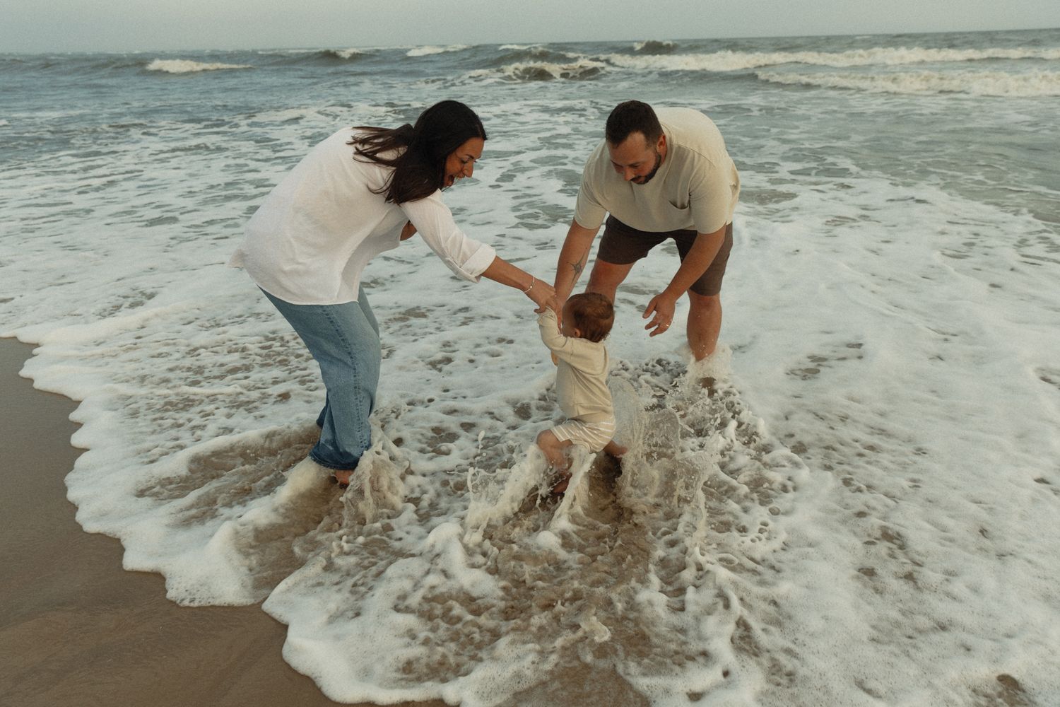 Couple playing in ocean waves at the beach during sunset.
