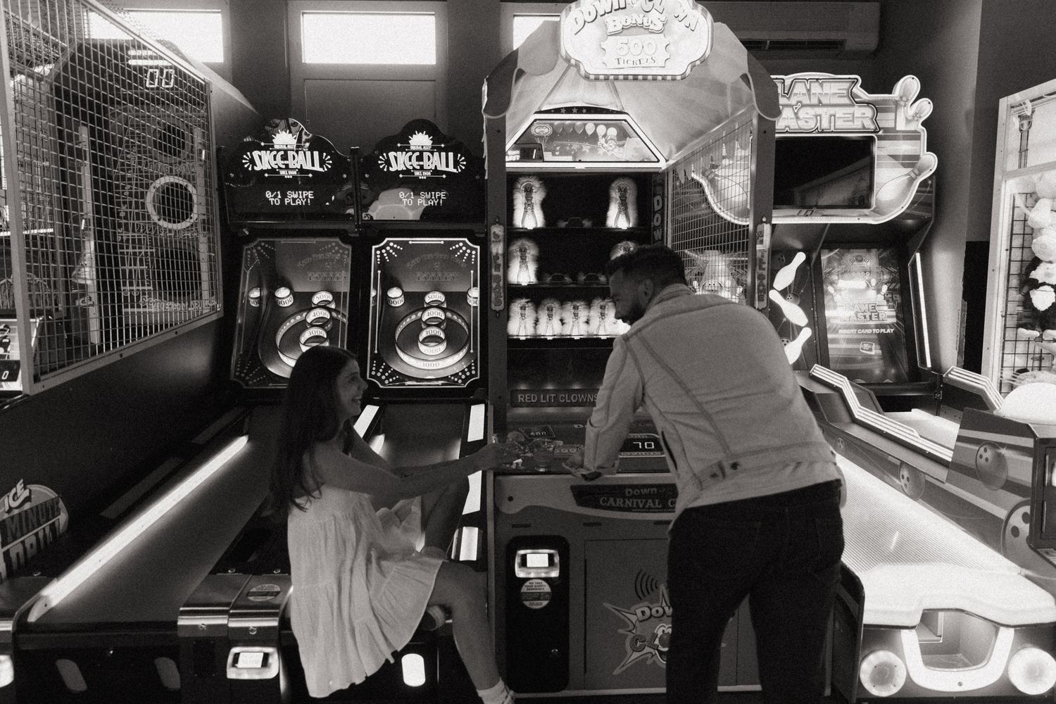Couple playing skee-ball and arcade games in black and white photography.