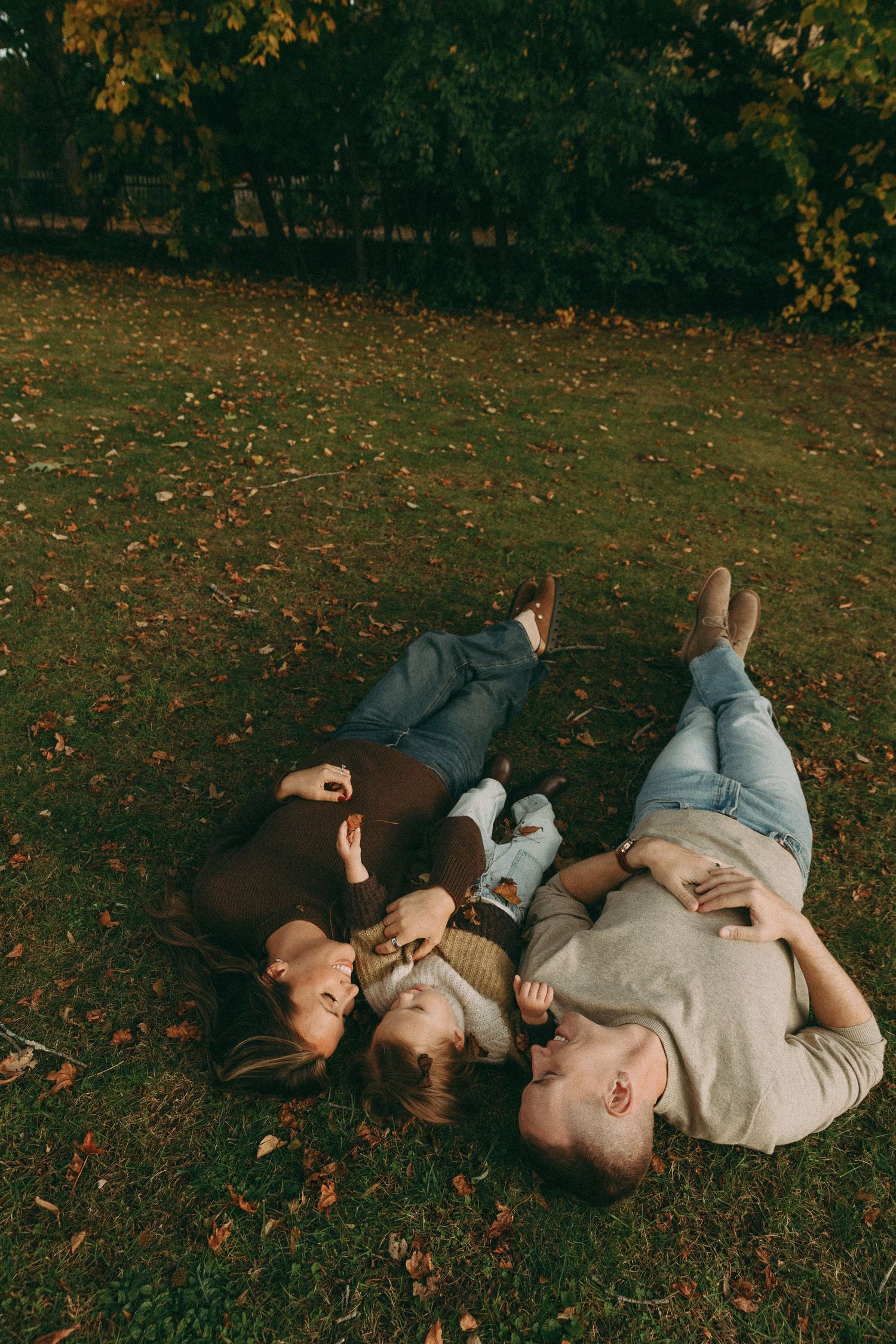 Family lying together on autumn grass surrounded by fallen leaves.