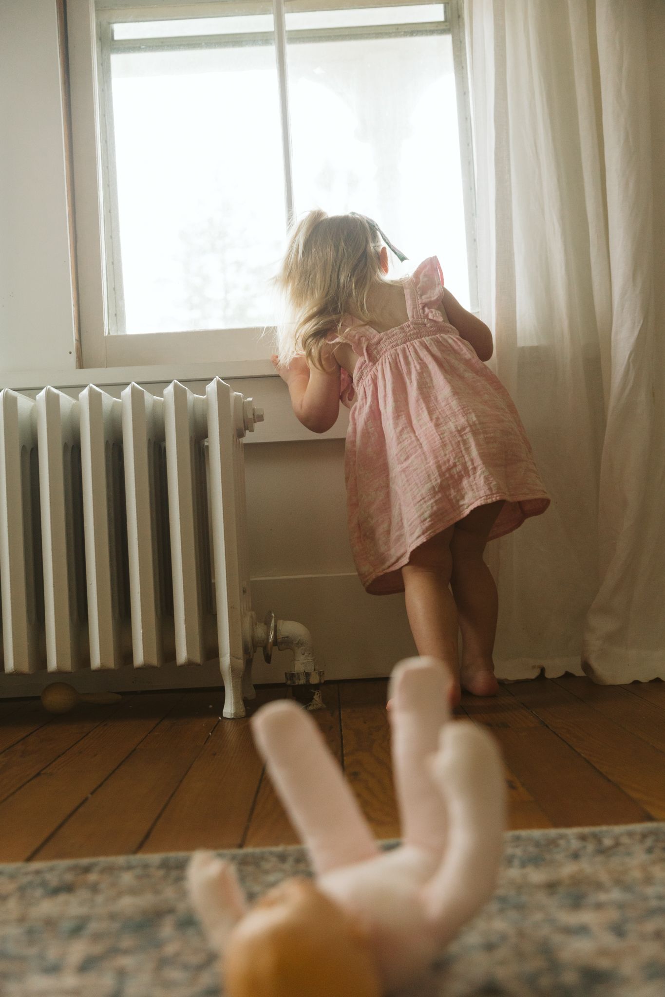 Pink dress twirling in motion against wooden floors near a window.
