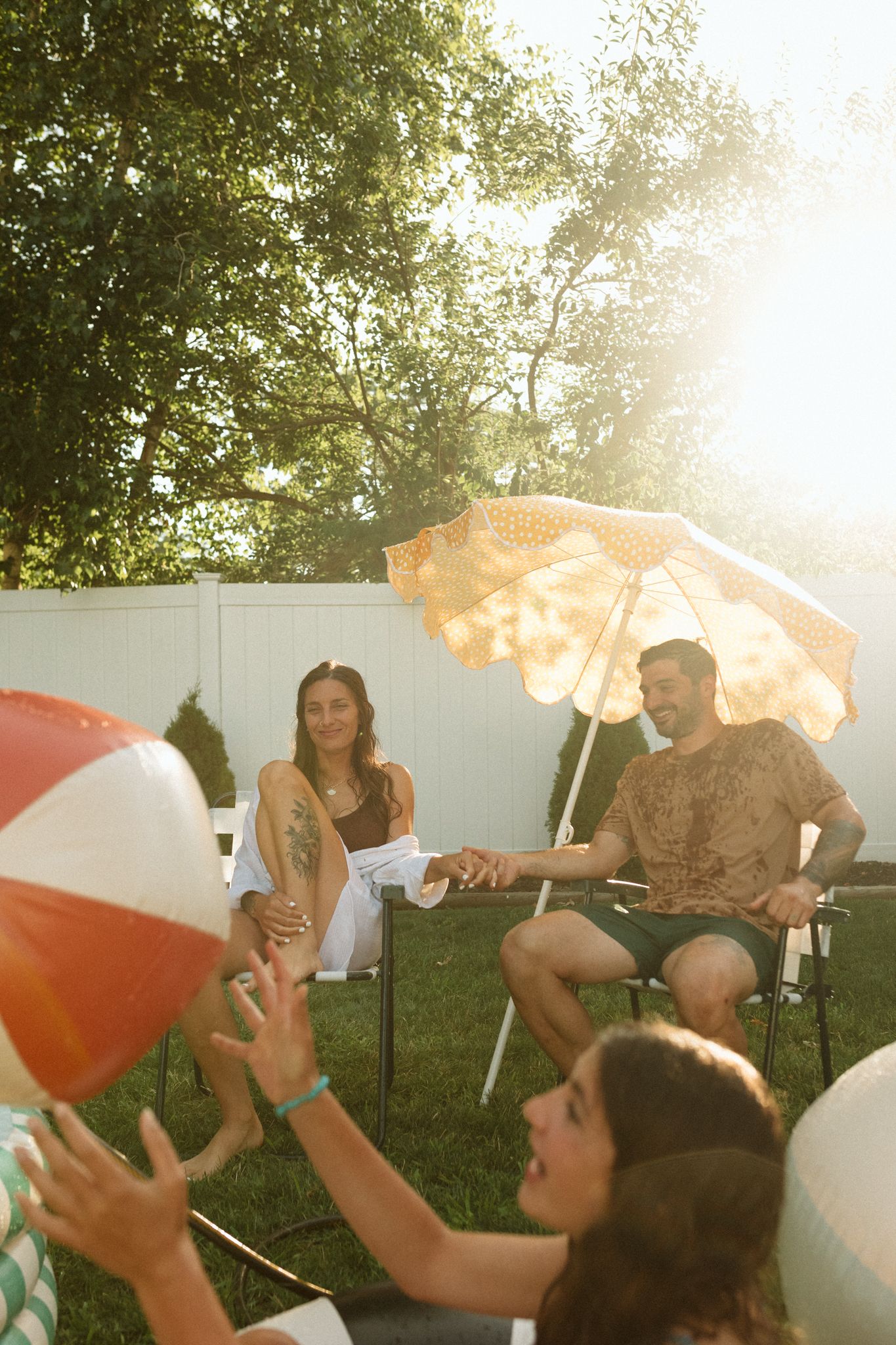Summer backyard gathering with beach balls and umbrellas in golden sunlight.