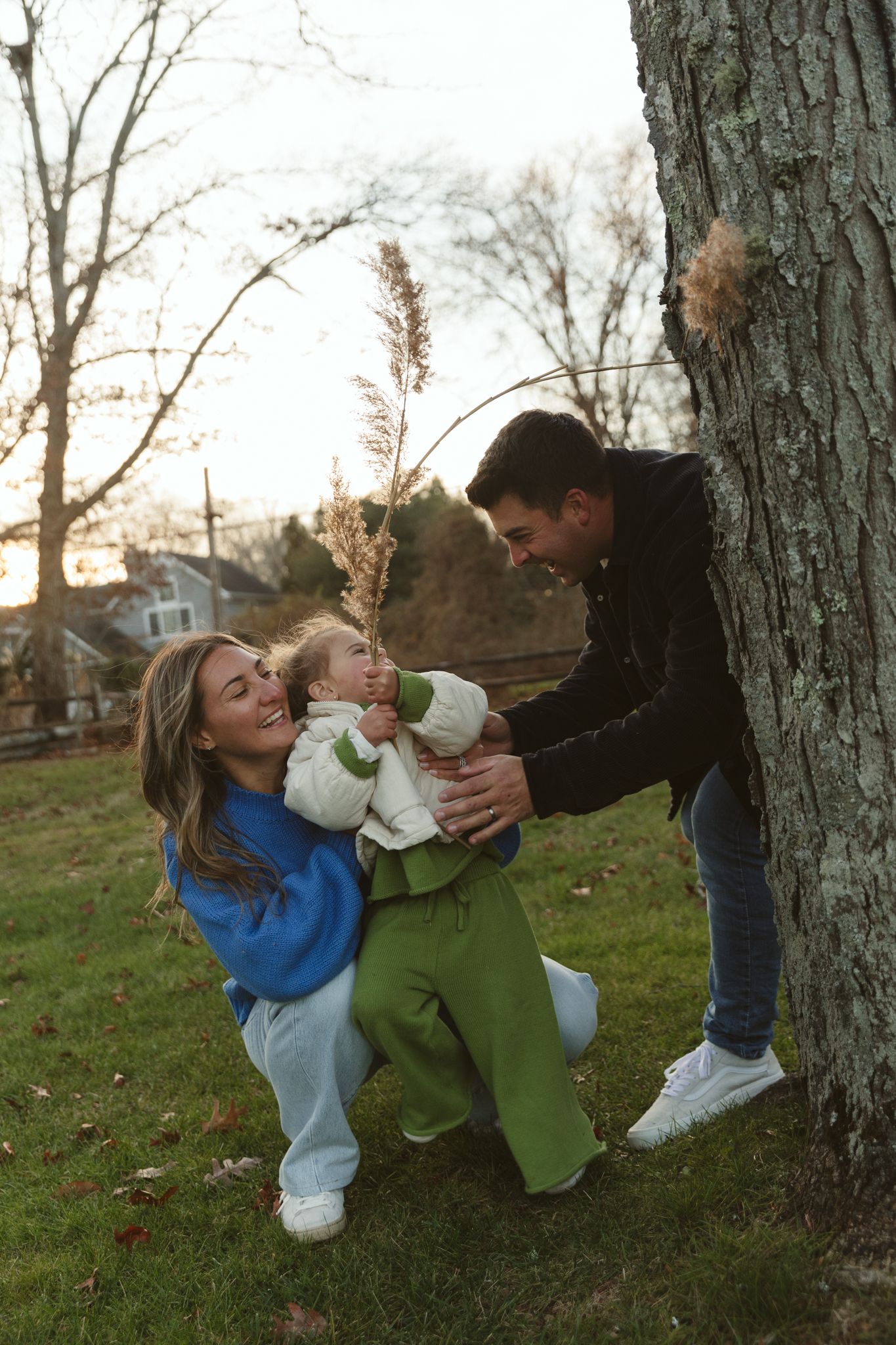 Playful family moment between trees in an autumn yard.