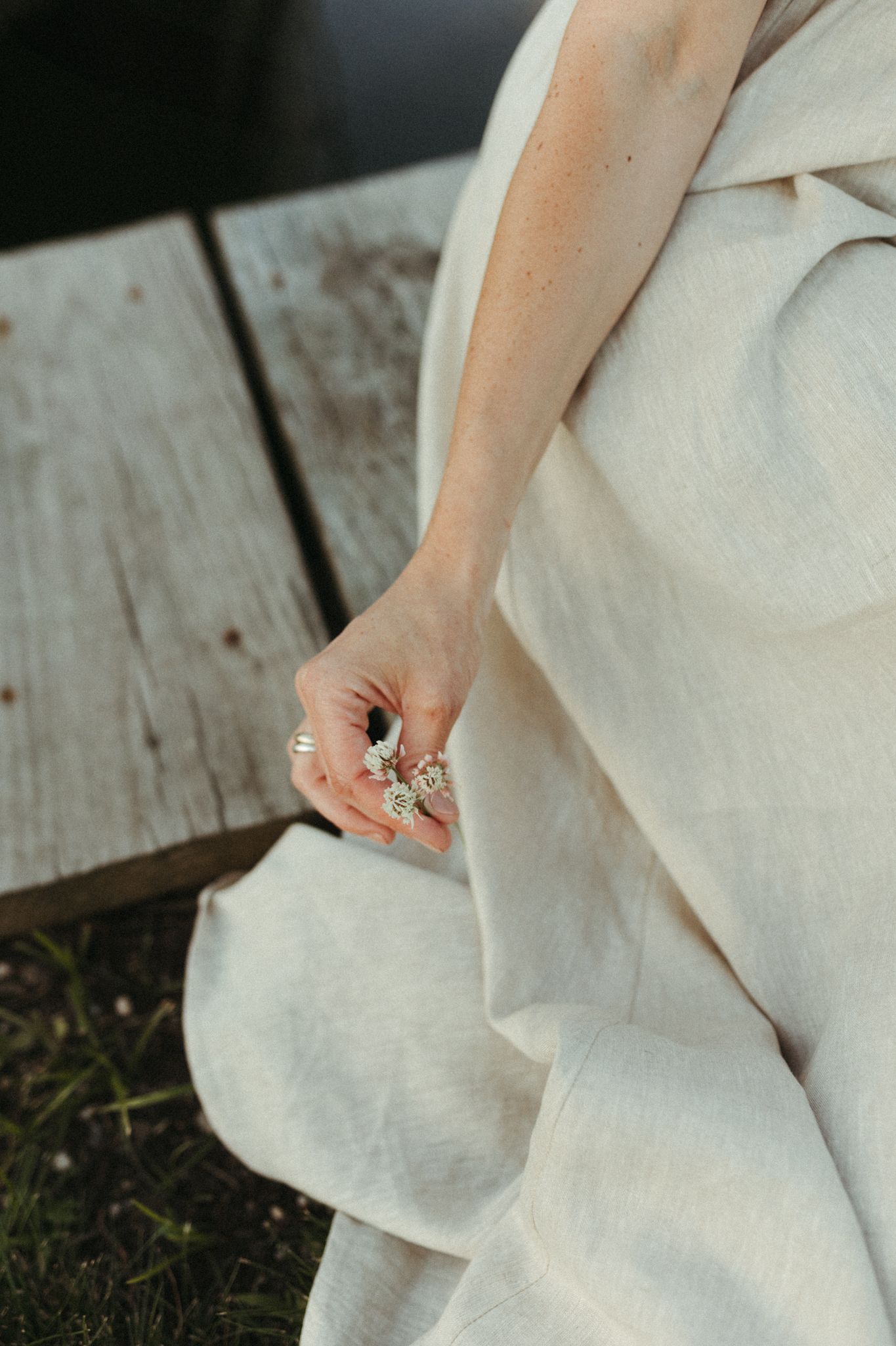 Detail shots of hands against a white dress on weathered wooden planks.