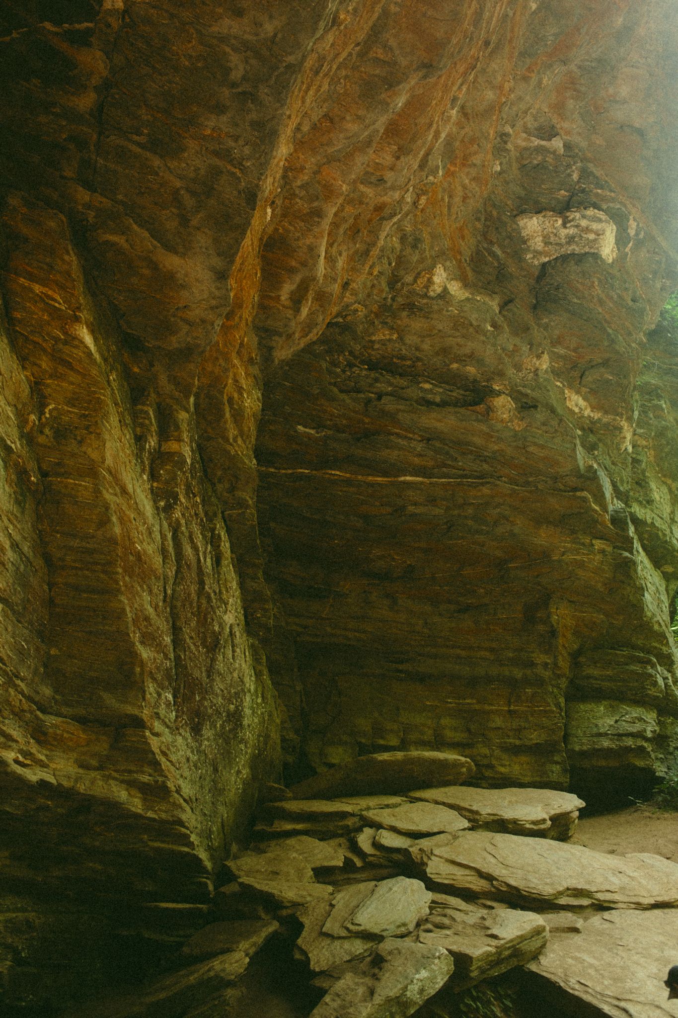 Dramatic sandstone cave interior with layered rock walls in warm amber tones and flat stone floor fragments.