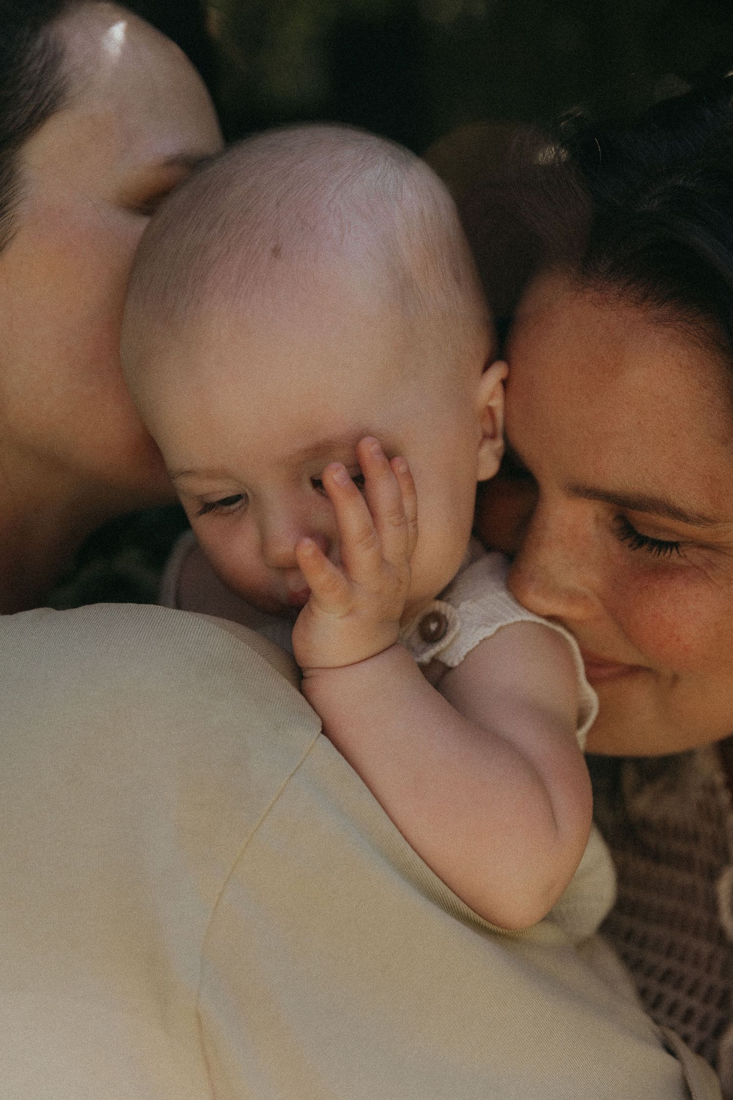 Two parents lovingly kissing their newborn baby on the cheeks in a tender moment.