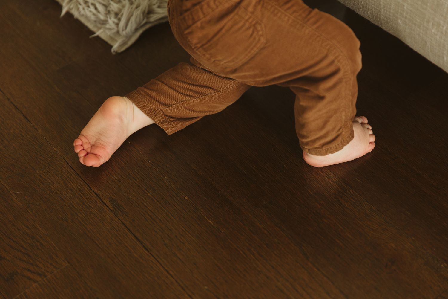 Bare feet and brown pants visible on dark hardwood flooring.