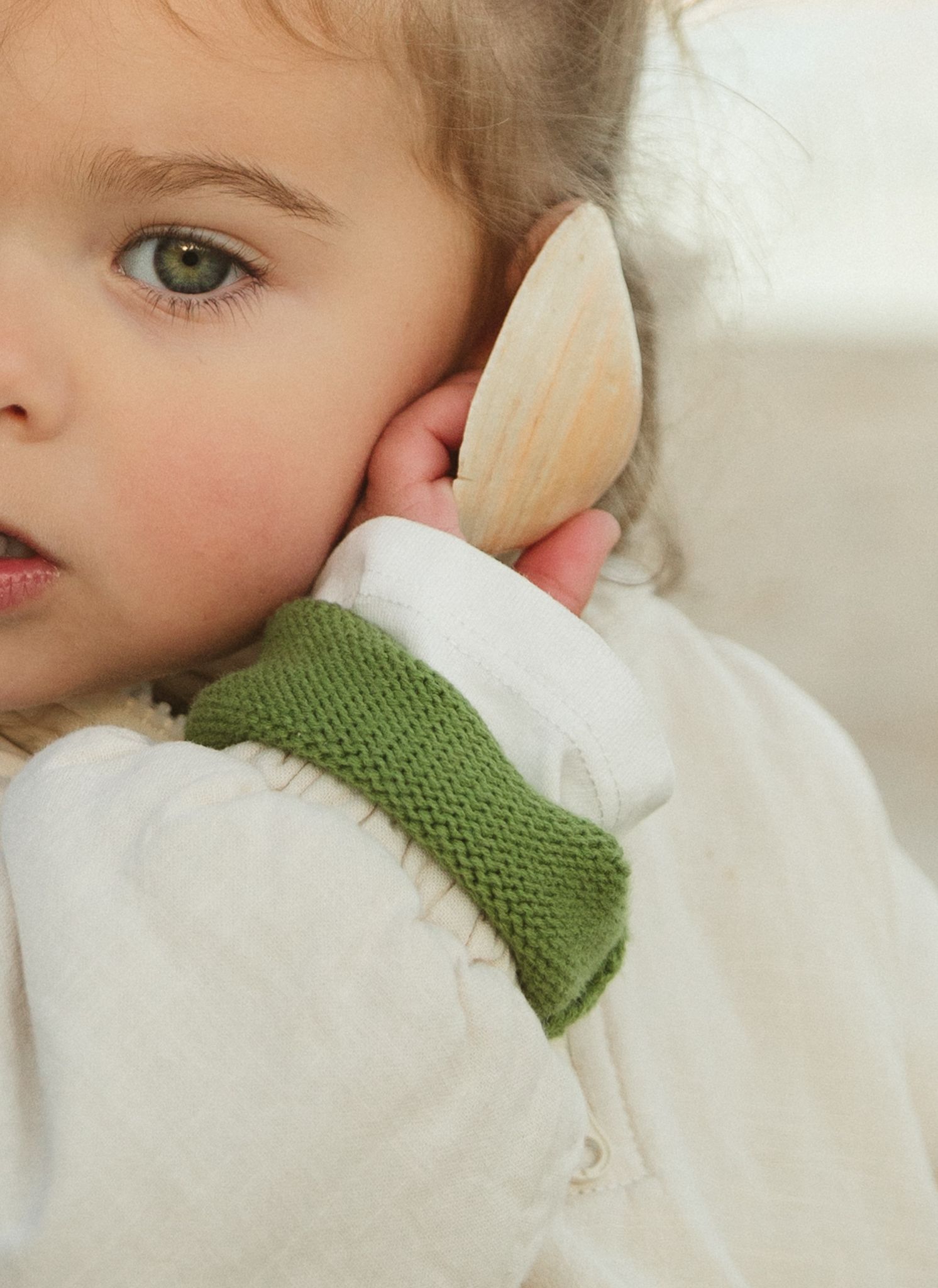Close-up view of a child wearing a white sweater with green knit collar.
