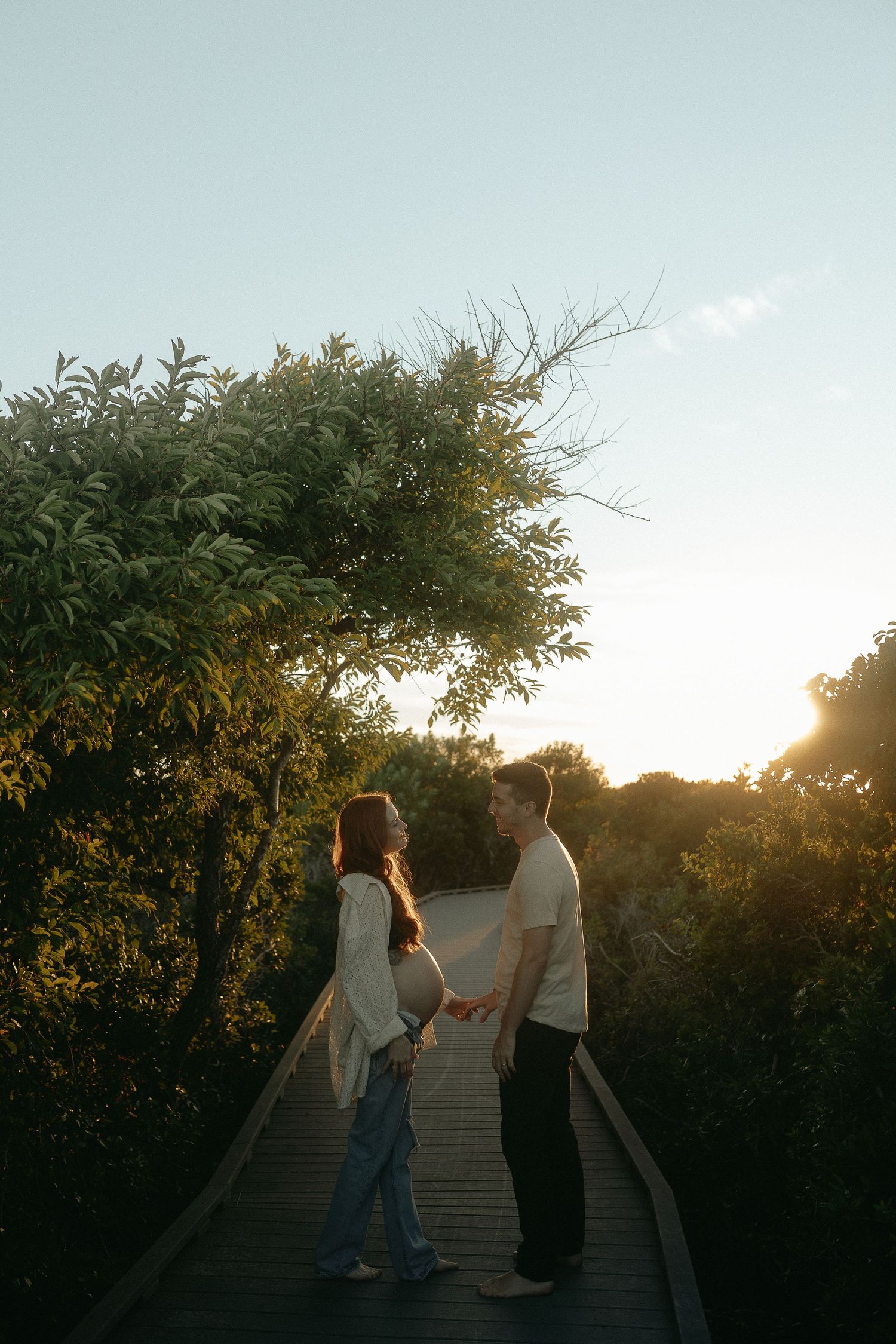 Couple walking up wooden boardwalk steps through lush foliage at sunset.