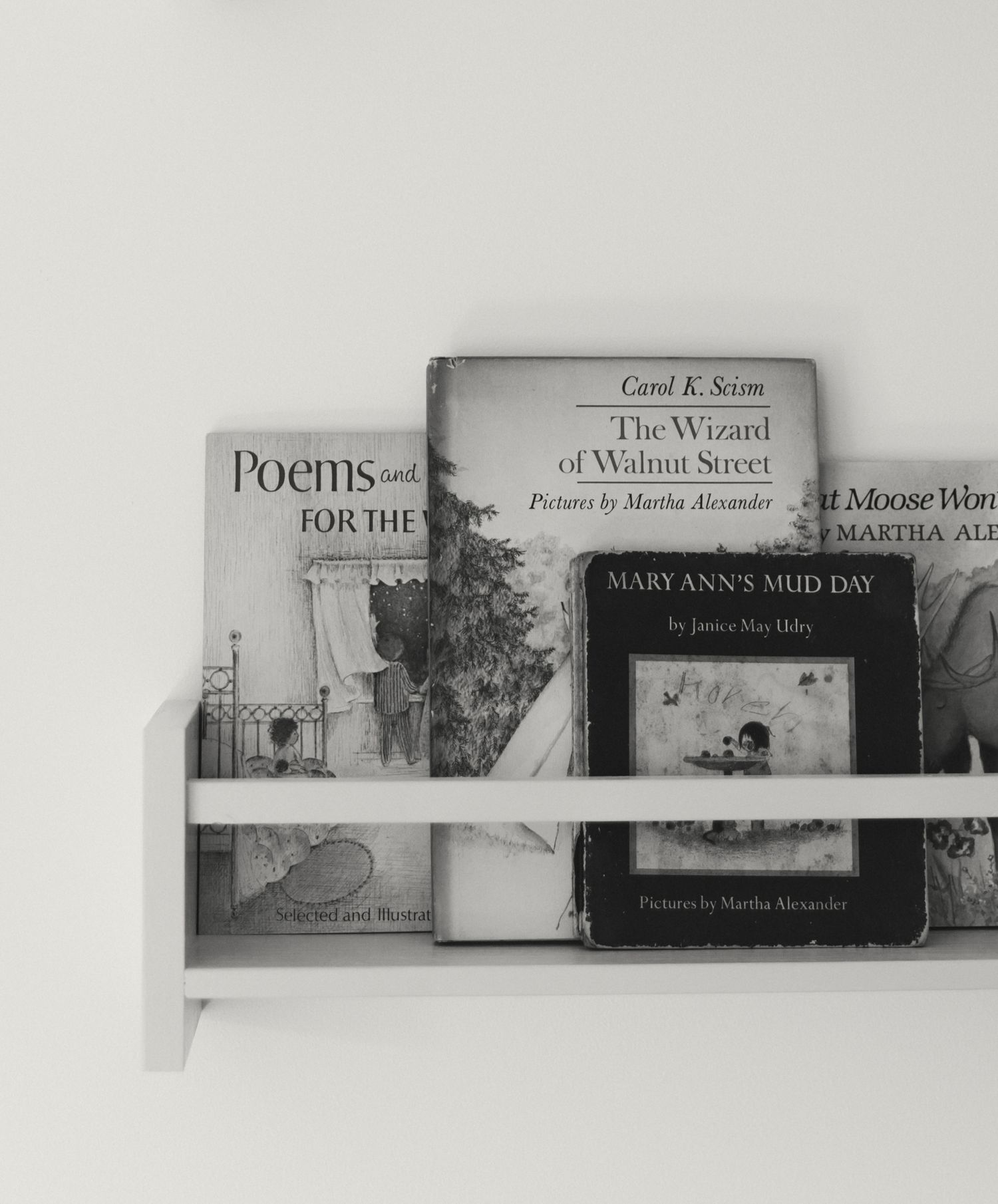 Row of children's books displayed on a floating shelf against a white wall.