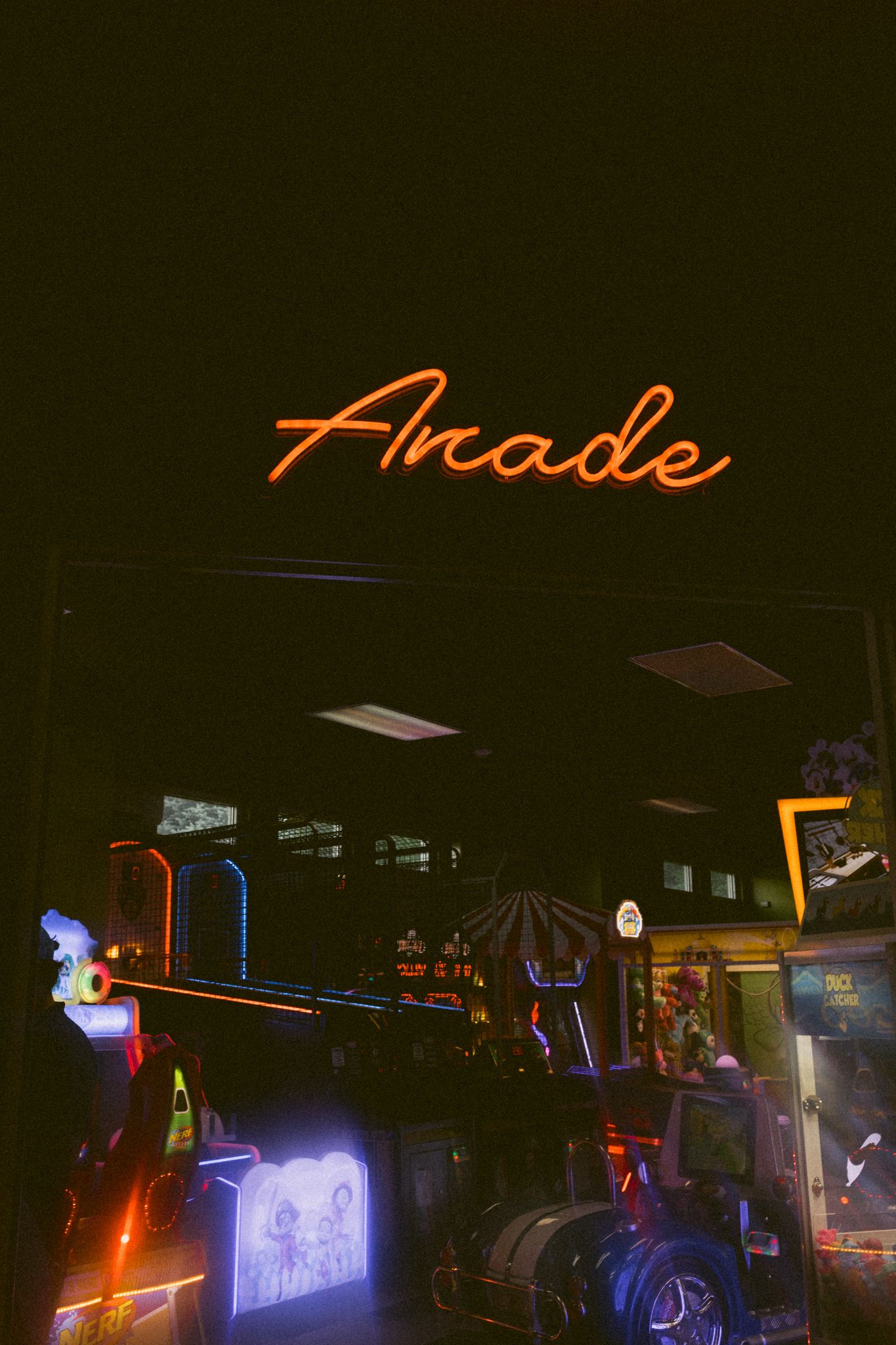 Glowing orange neon Arcade sign above colorful arcade machines in dark venue.
