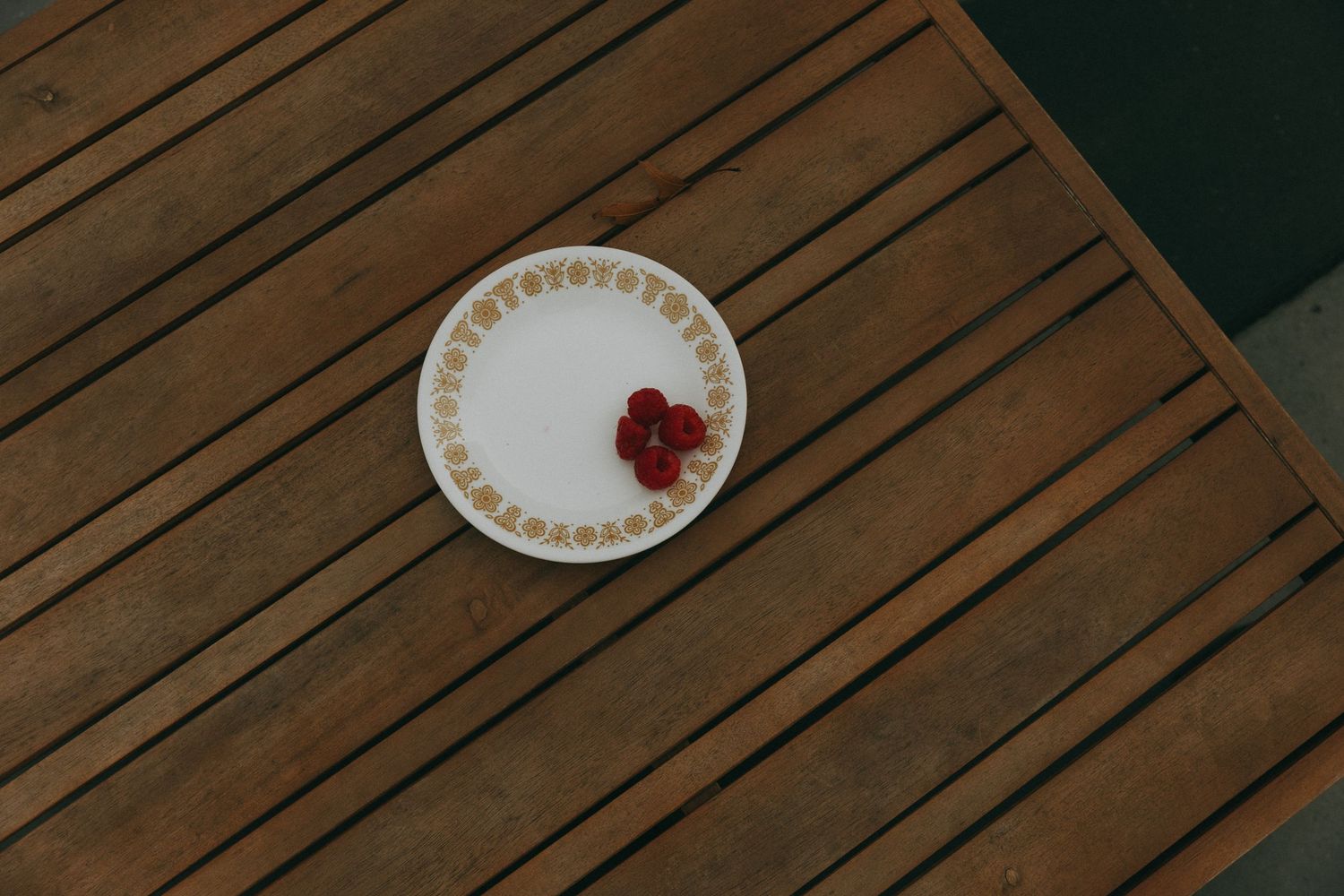 White decorative plate with raspberries centered on wooden slatted outdoor table.