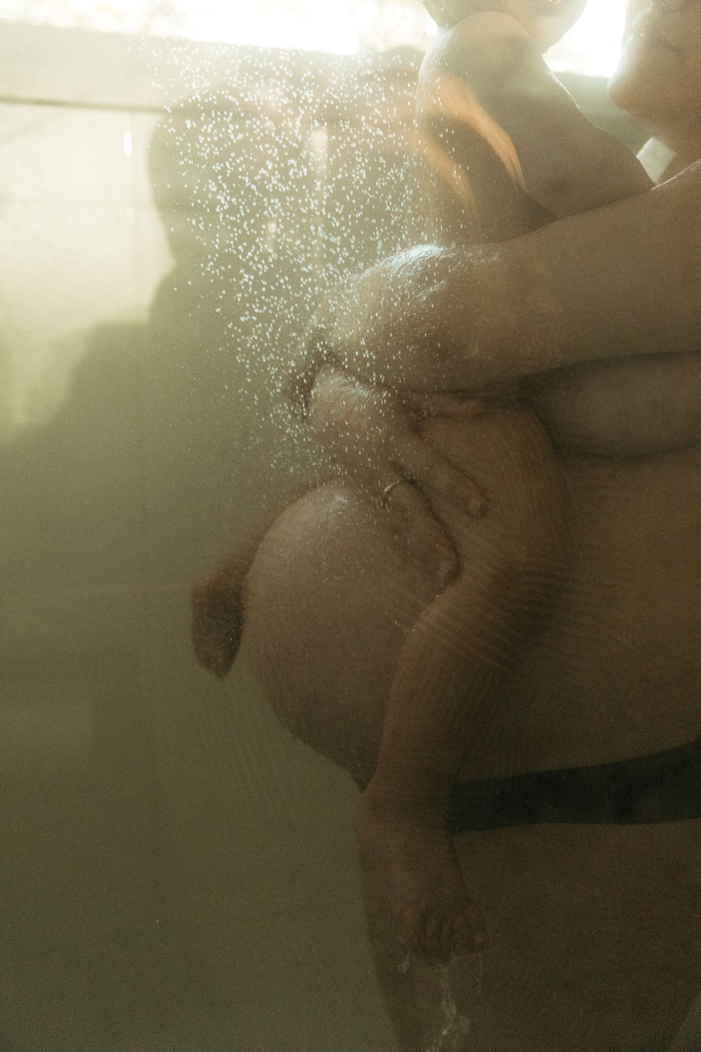 Close-up underwater shot of a pregnant woman's baby bump with water droplets in soft golden light.