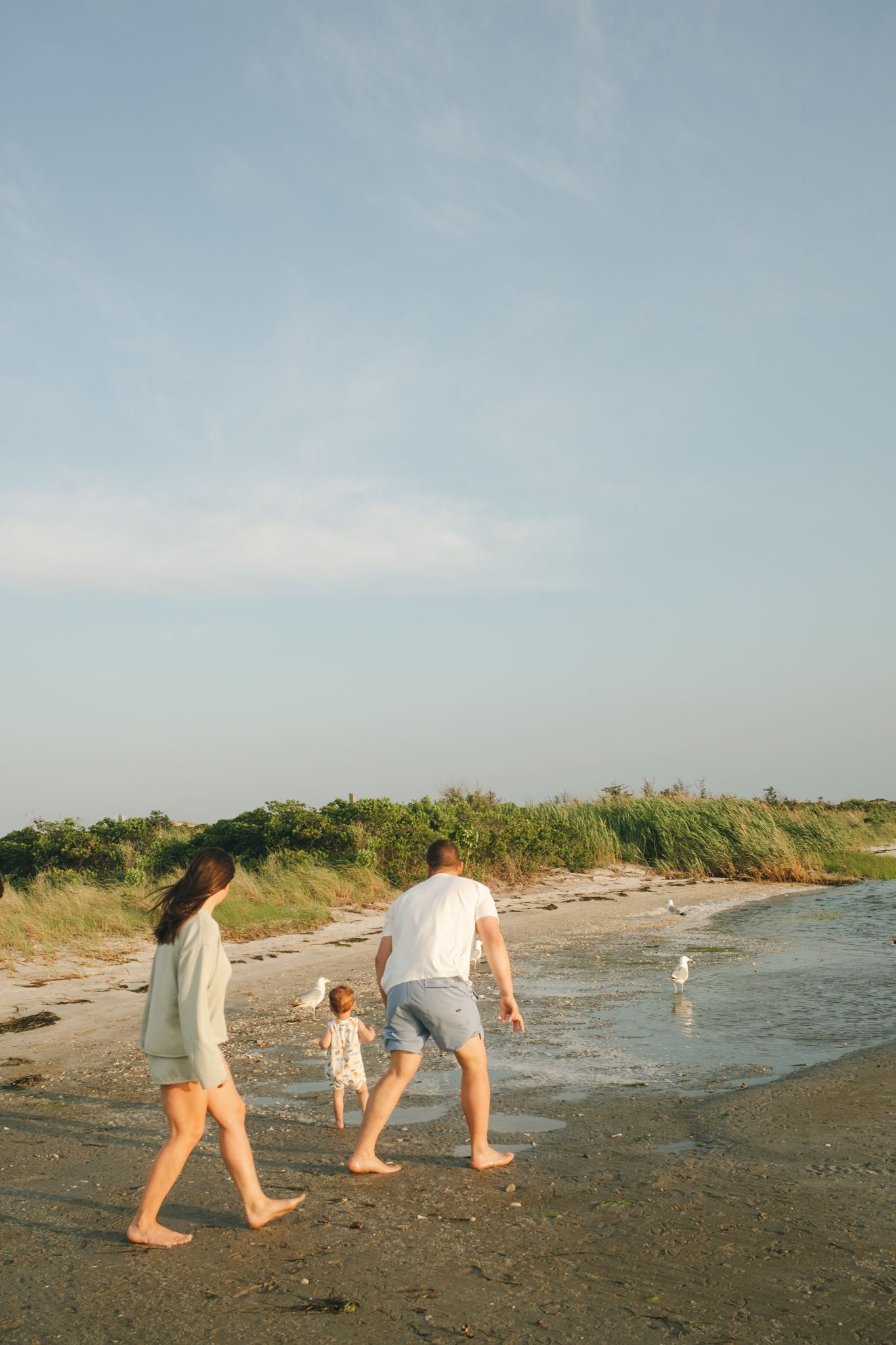 Family takes leisurely stroll along shoreline during golden hour.