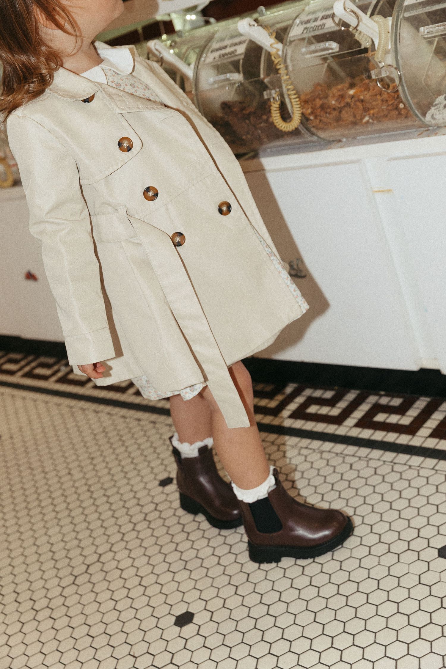 Beige trench coat and brown boots shown against hexagonal tile flooring.