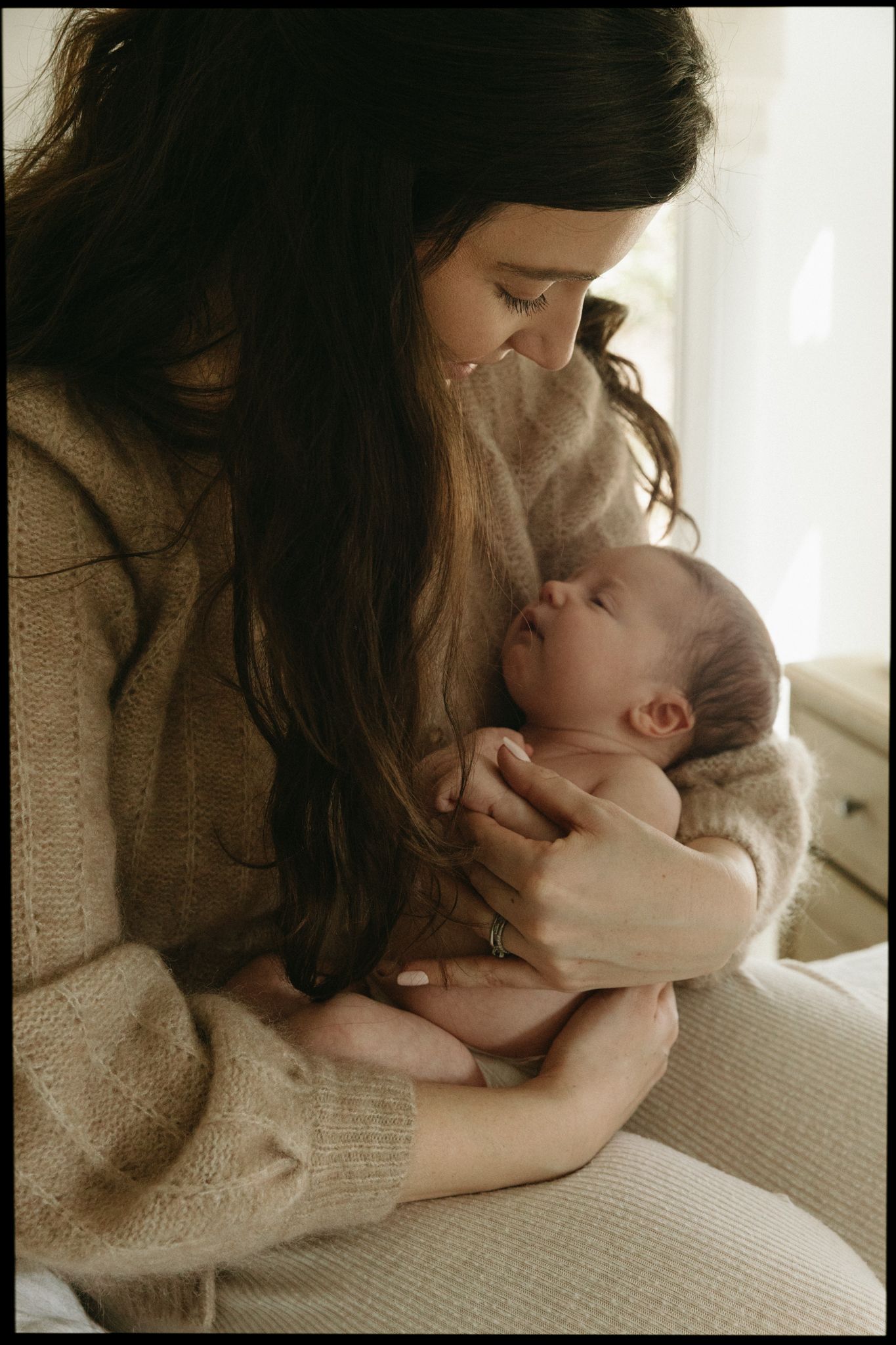 Intimate portrait of parent and baby sharing a loving moment in soft beige tones.