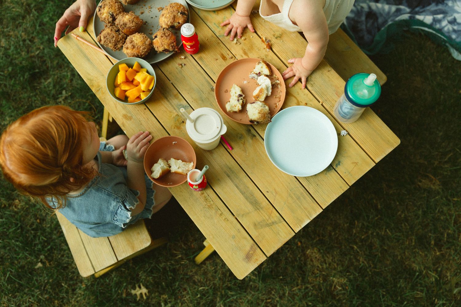 Overhead view of a wooden picnic table outdoors with plates of food and drinks.