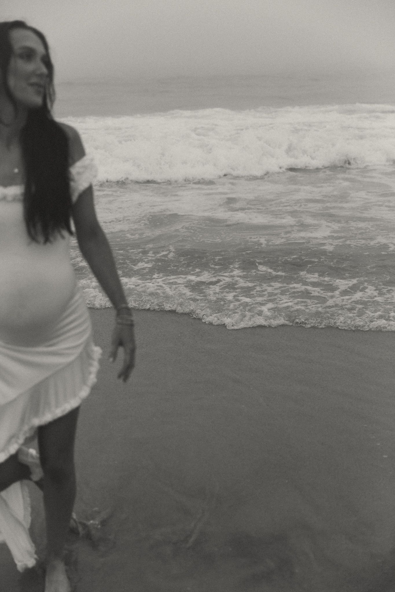 Person in white dress walking joyfully along the beach shoreline.