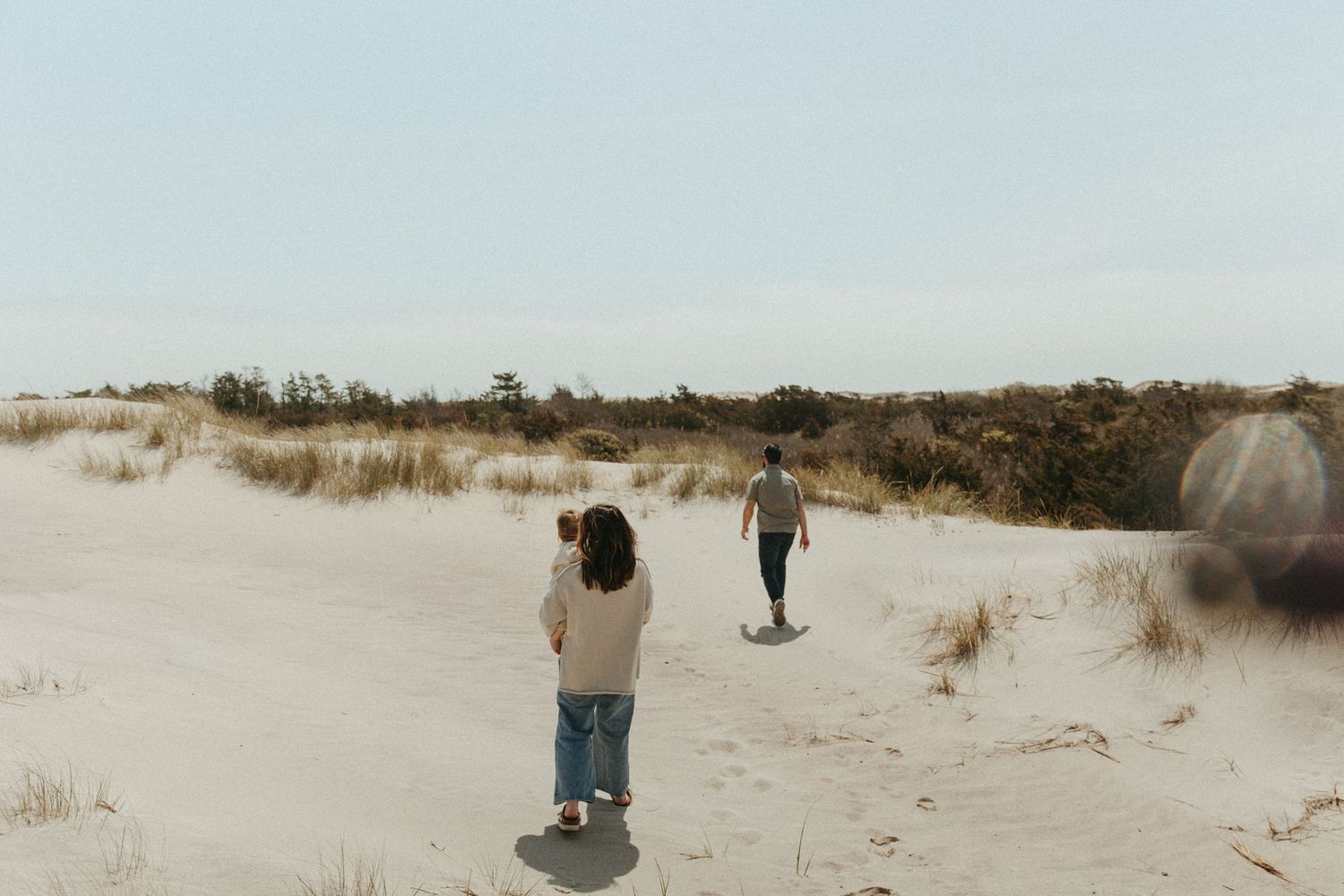 People walking through sandy coastal dunes on a clear day.