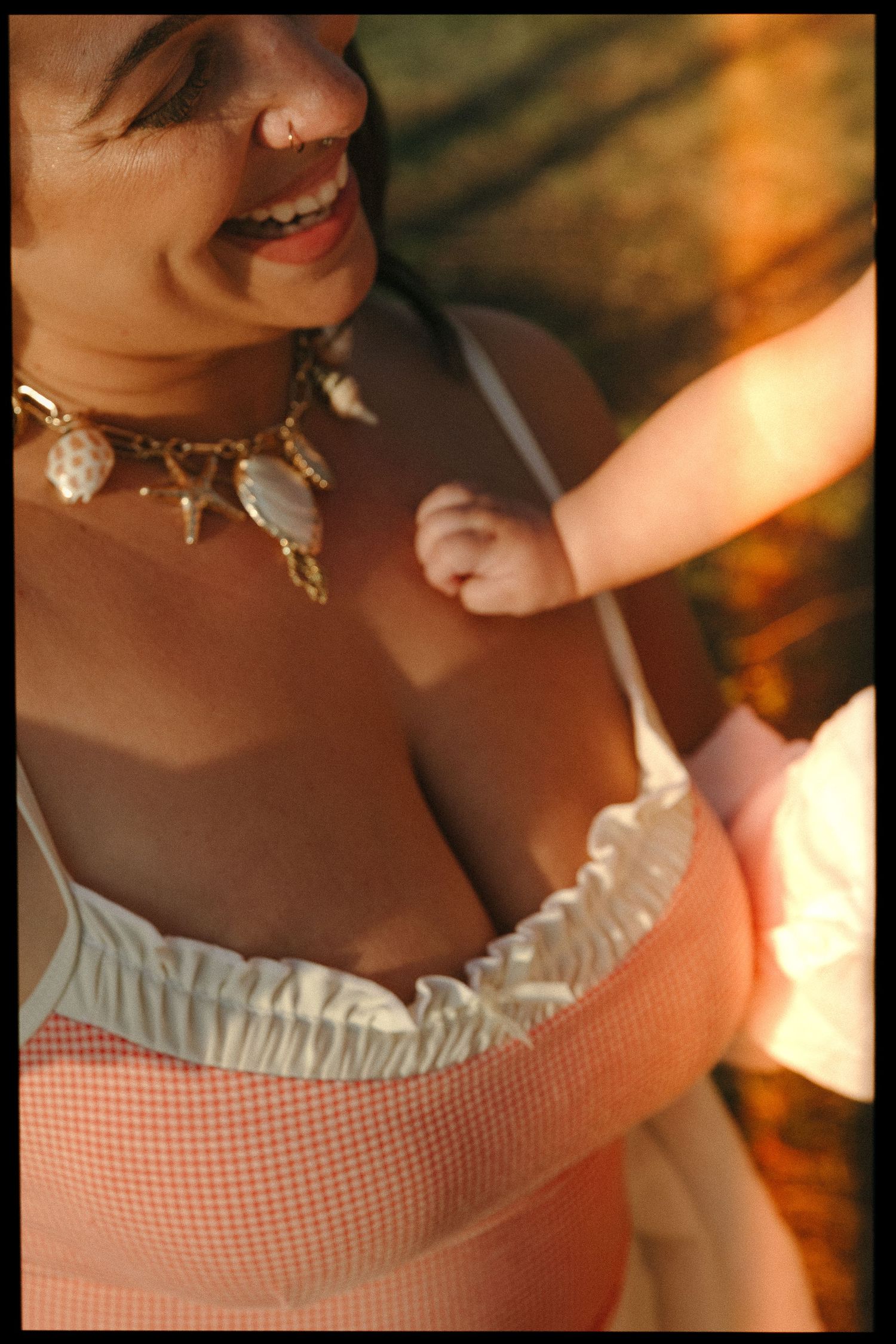 Smiling woman wearing a peach top and gold shell necklace in warm golden sunlight.