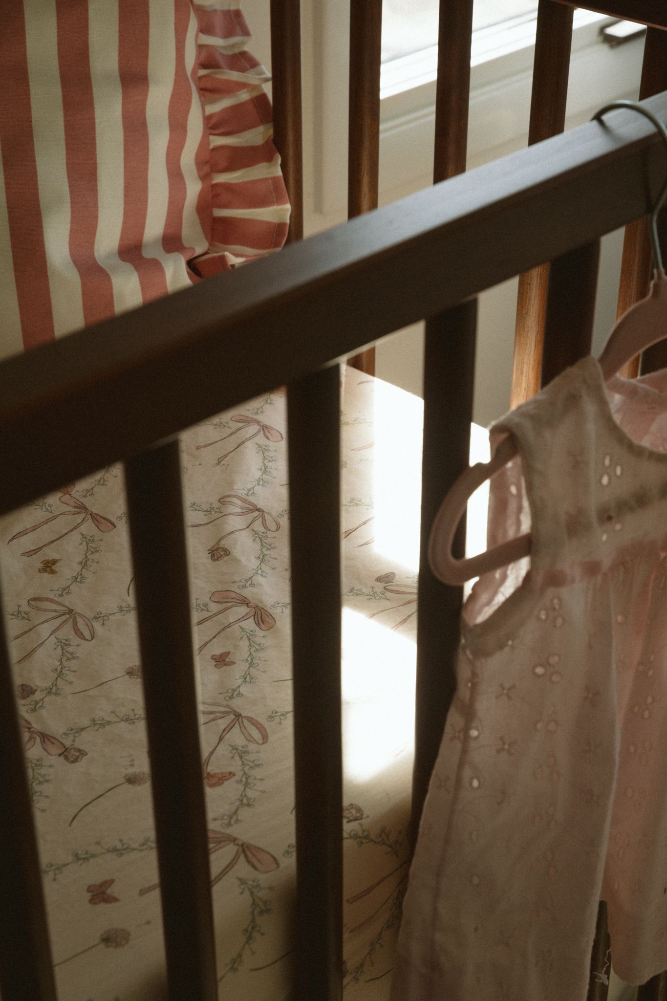 Wooden crib rails with pink and white striped bedding details.