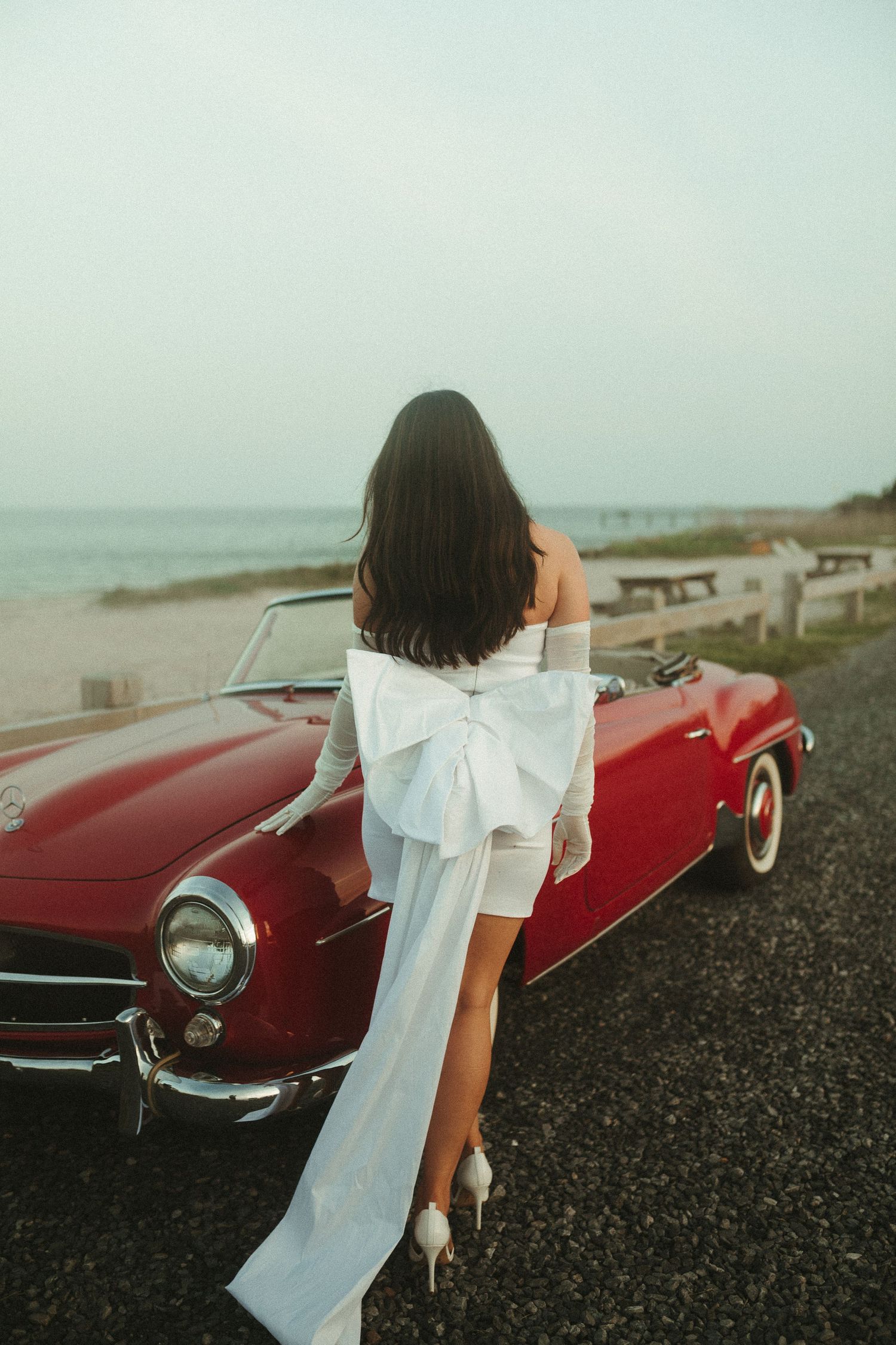 Classic red convertible car parked on a coastal road with flowing white fabric.