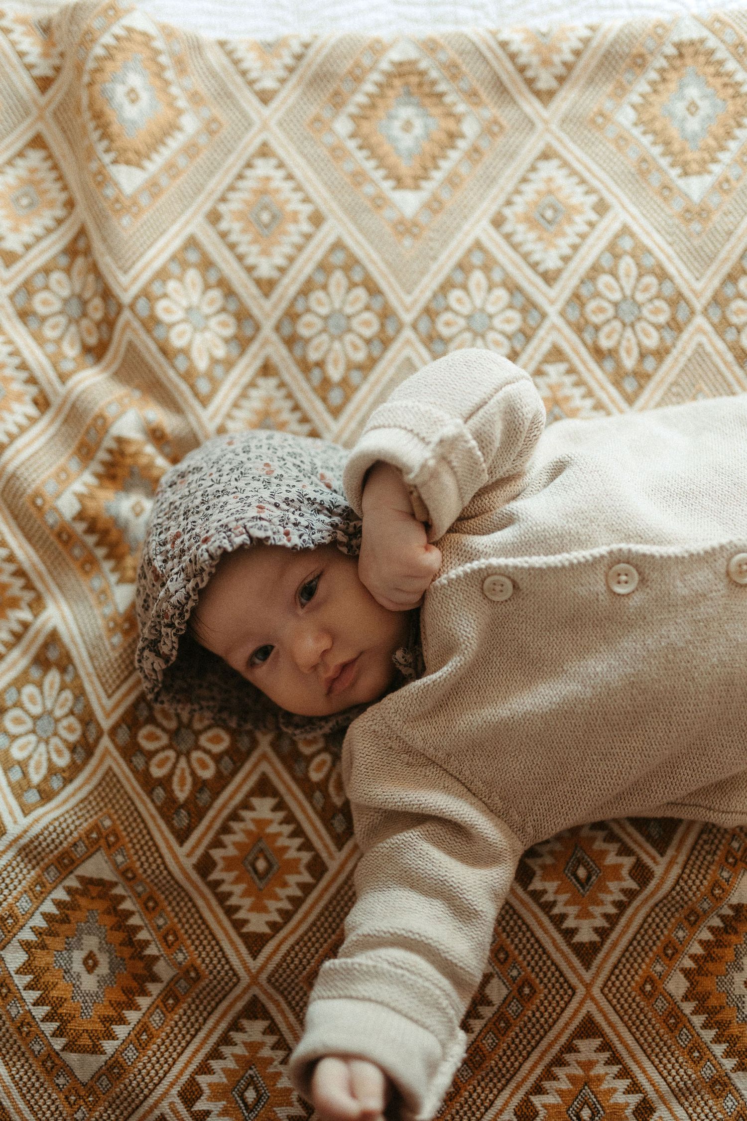 Baby lying on patterned beige fabric with geometric designs.