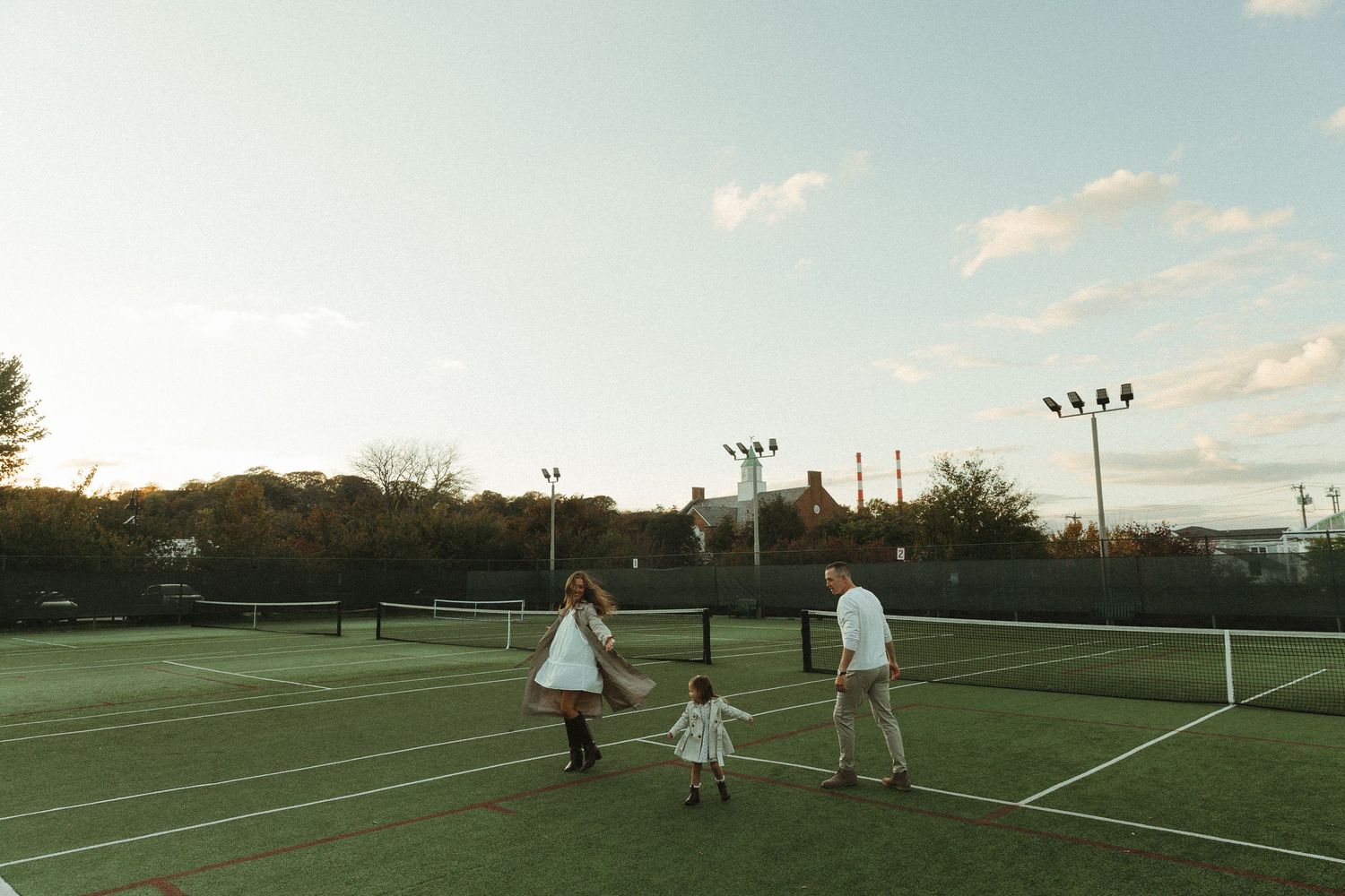 Wide panoramic view of tennis courts and players at sunset.