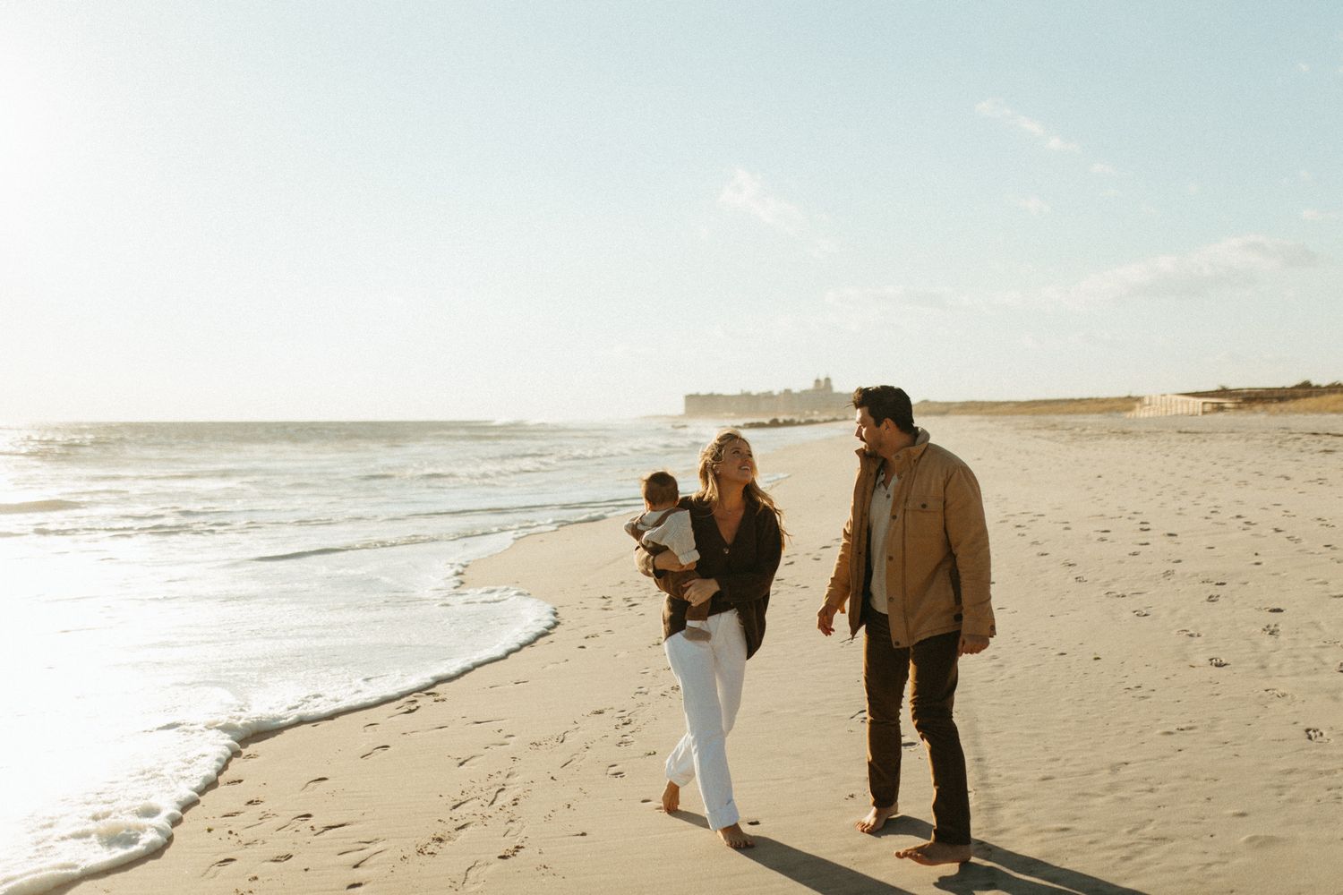 A panoramic beach scene with figures walking along the sandy shore at dusk.