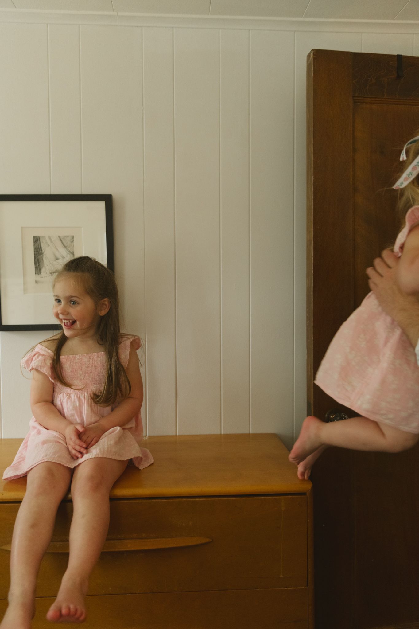 Someone in pink sitting on wooden furniture in a bright room with white walls.