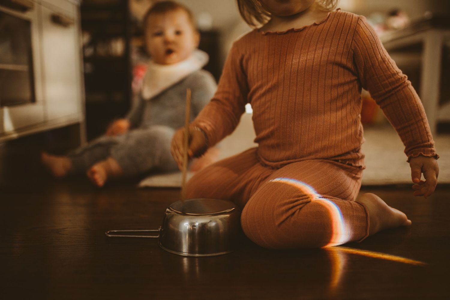 Child in brown clothing sitting on floor in warm lighting.