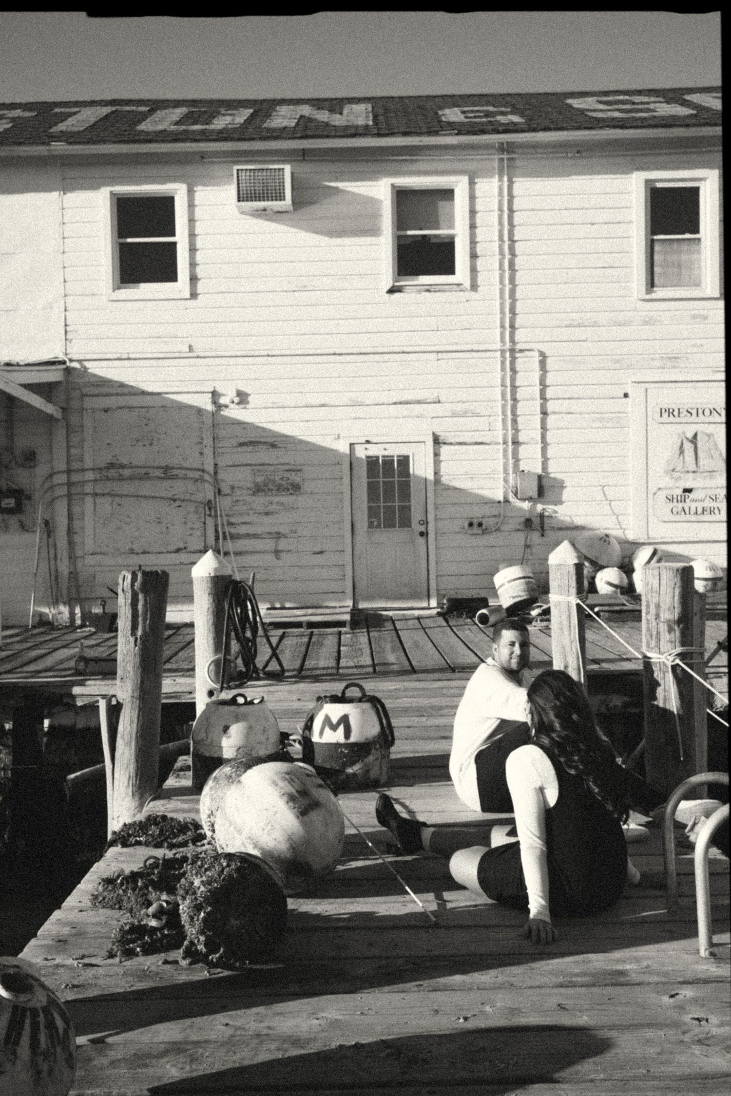 Black and white exterior view of white industrial buildings with parked cars.