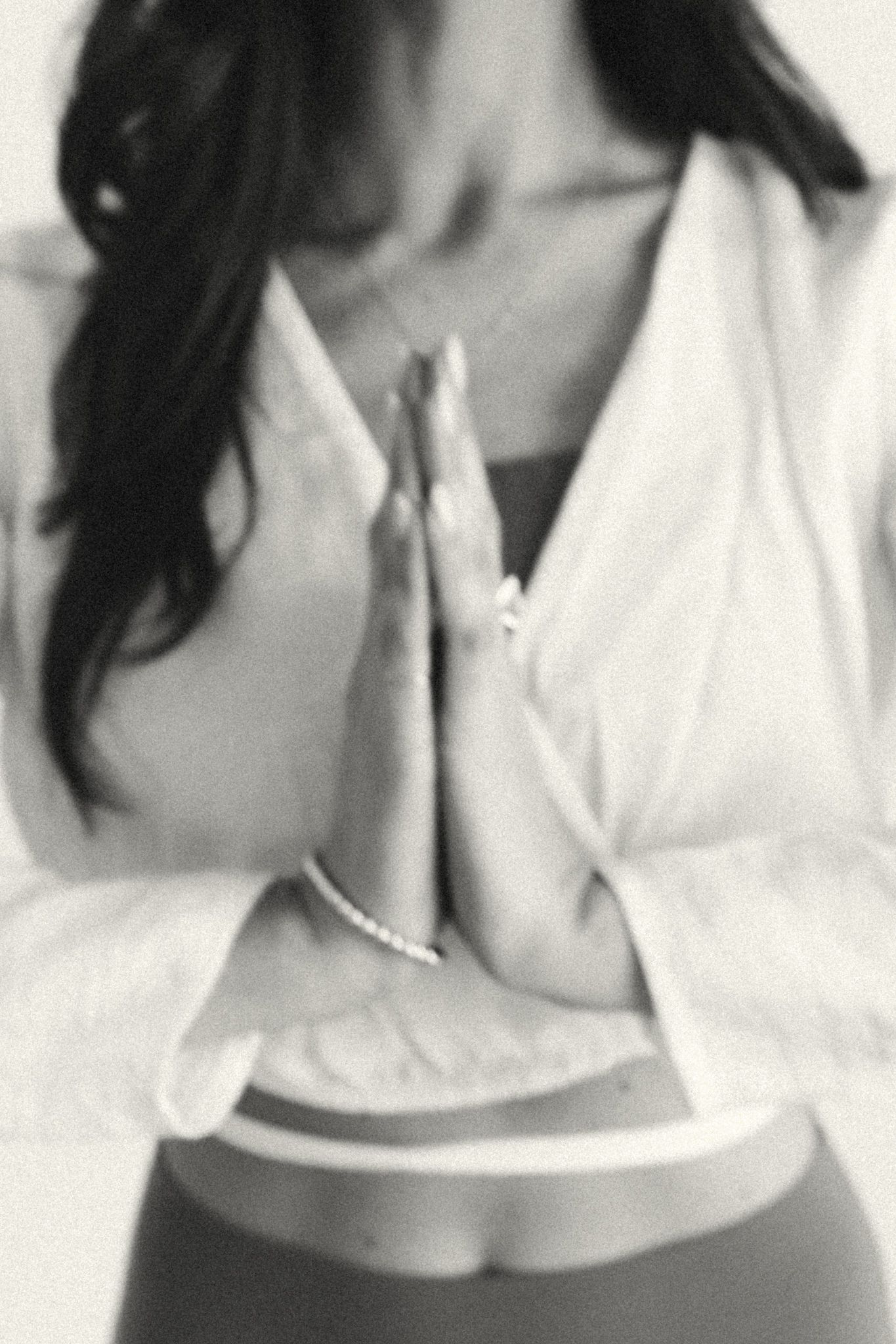 Black and white photo of a woman in prayer pose wearing a white jacket and bracelet, practicing yoga or meditation.